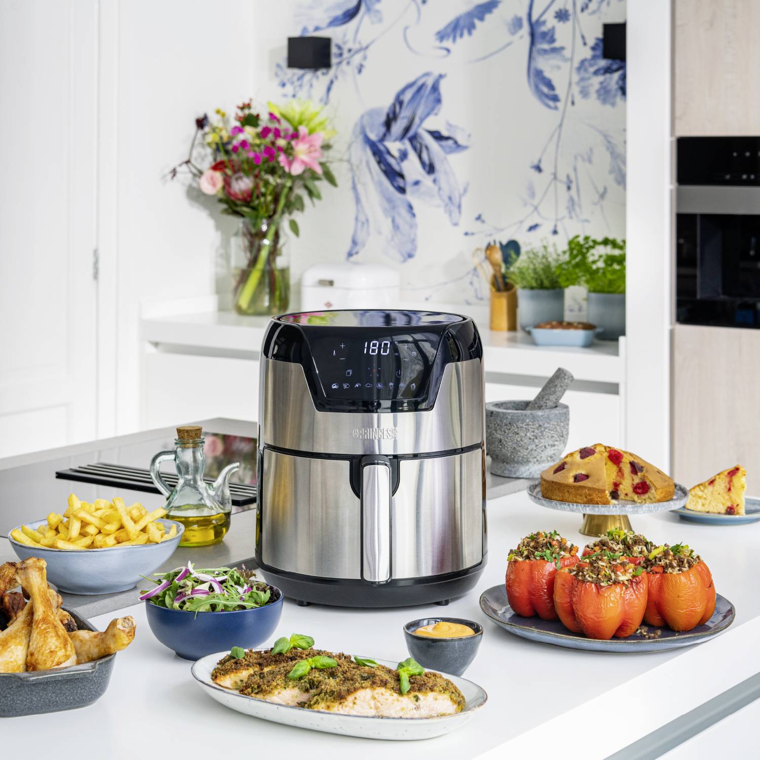 Una cucina moderna con un'airfryer, circondato da pietanze preparate come patatine fritte, peperoni ripieni e insalata su un tavolo.