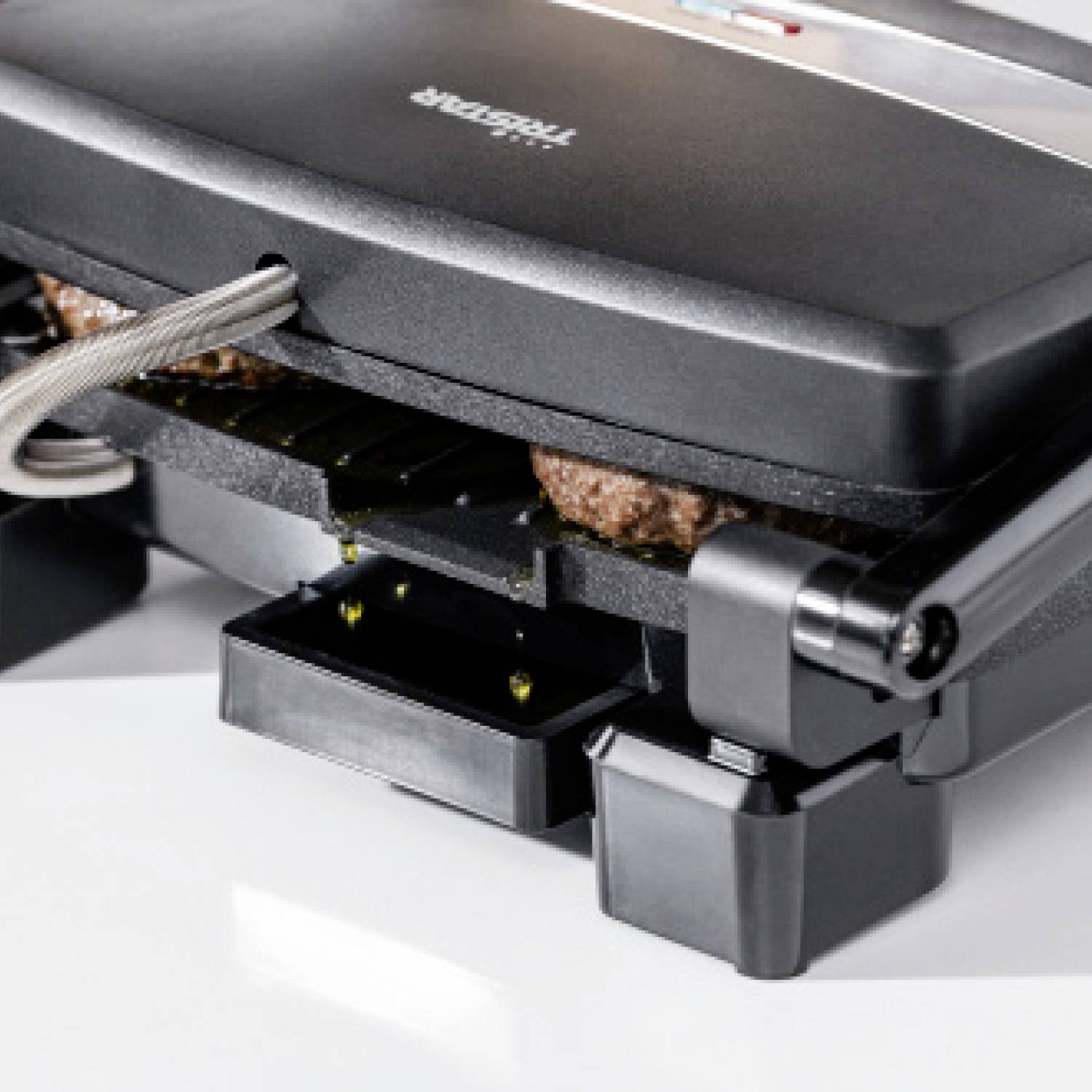 Una piastra per panini che sta grigliando due hamburger. La griglia è parzialmente aperta e mostra i pezzi di carne tra le piastre.