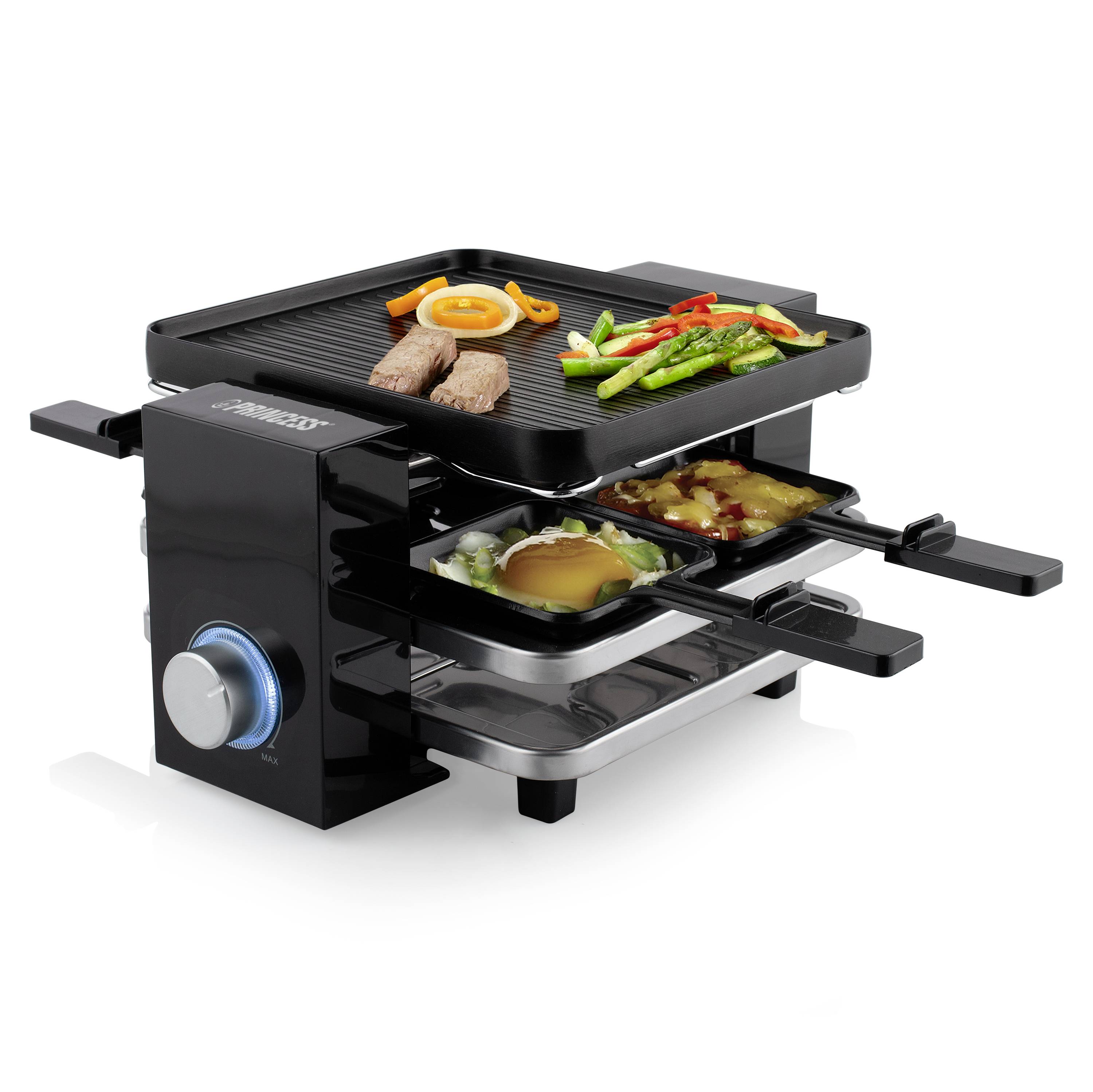 Un dispositivo per raclette nero con piastra per grigliare sulla parte superiore e due piccole padelle sottostanti. Padelle con uova e verdure.