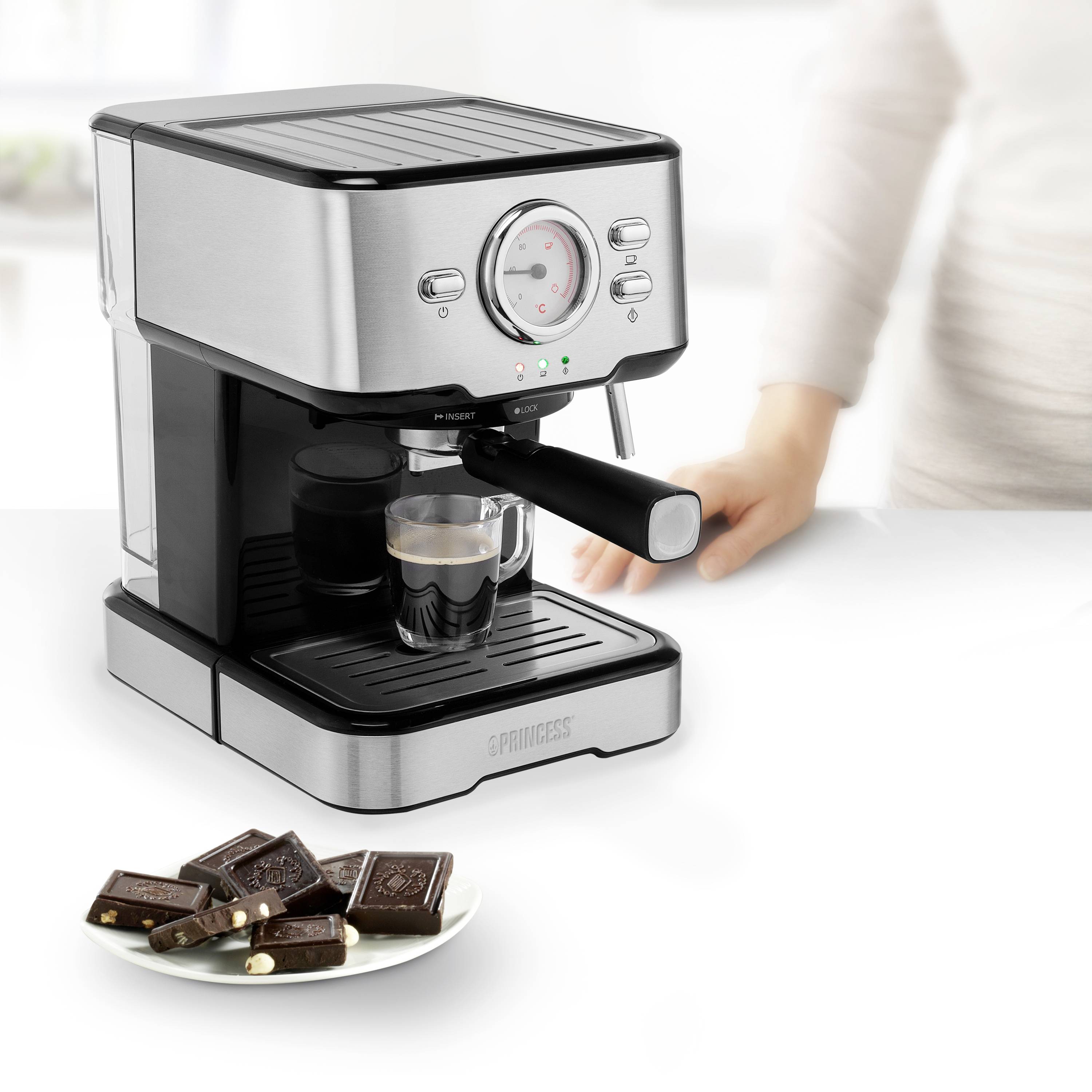 Macchina per espresso con una tazza di espresso, una mano accanto. Su un piatto davanti ci sono pezzi di cioccolato.