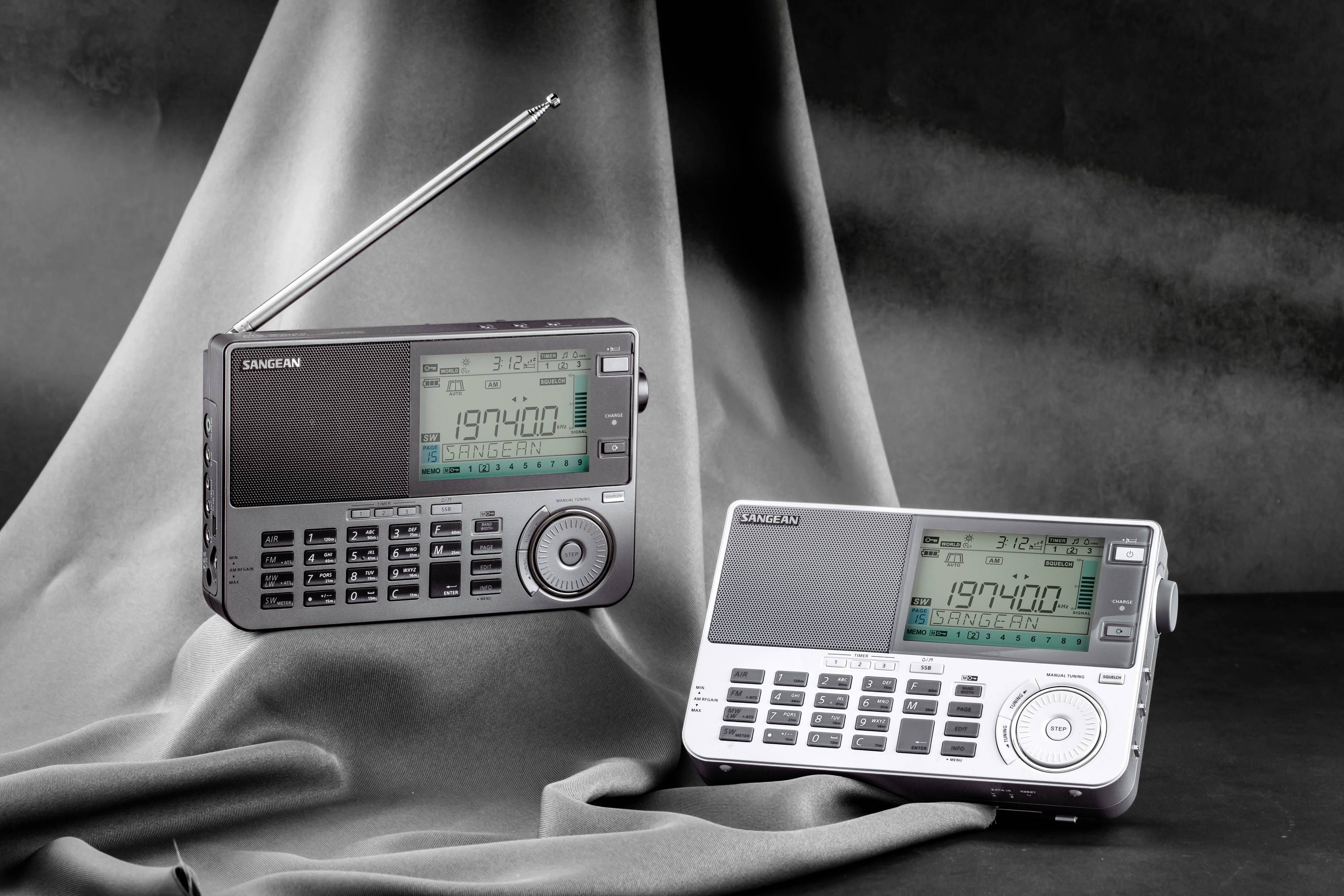 Due radio portatili sono poggiate su uno sfondo di tessuto grigio. Entrambe mostrano la frequenza '197400' sui loro display.