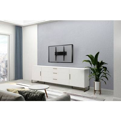 Soggiorno semplicemente arredato con un mobile credenza bianco, televisore montato a parete senza schermo e una pianta verde. Sullo sfondo, una vista della città dalla finestra.
