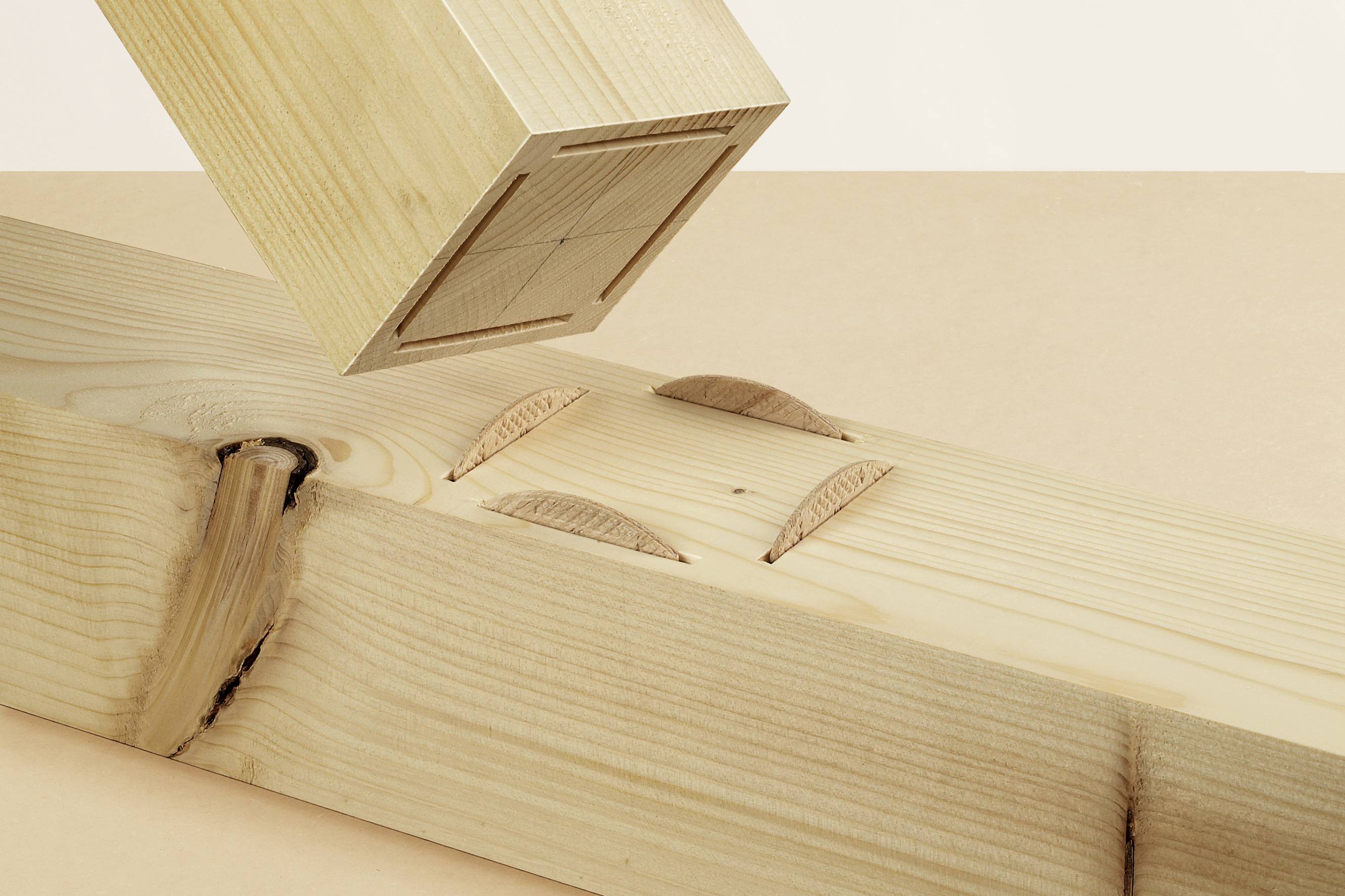 Un trave di legno con due spine di legno inserite accanto a un blocco con un'apposita scanalatura. Rappresentazione di un metodo di giunzione del legno.