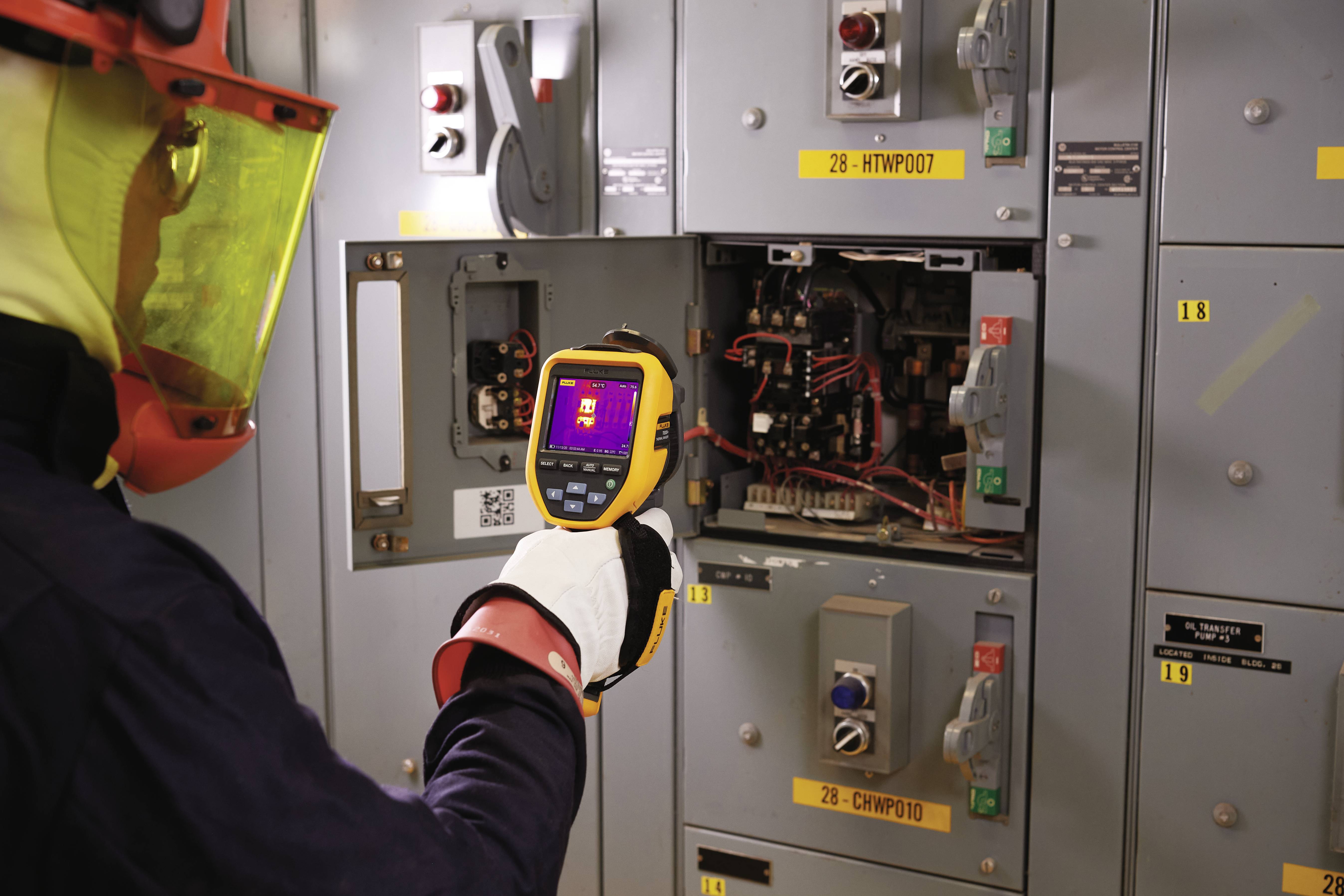 Una persona con indumenti protettivi utilizza una termocamera per verificare la temperatura degli impianti elettrici.