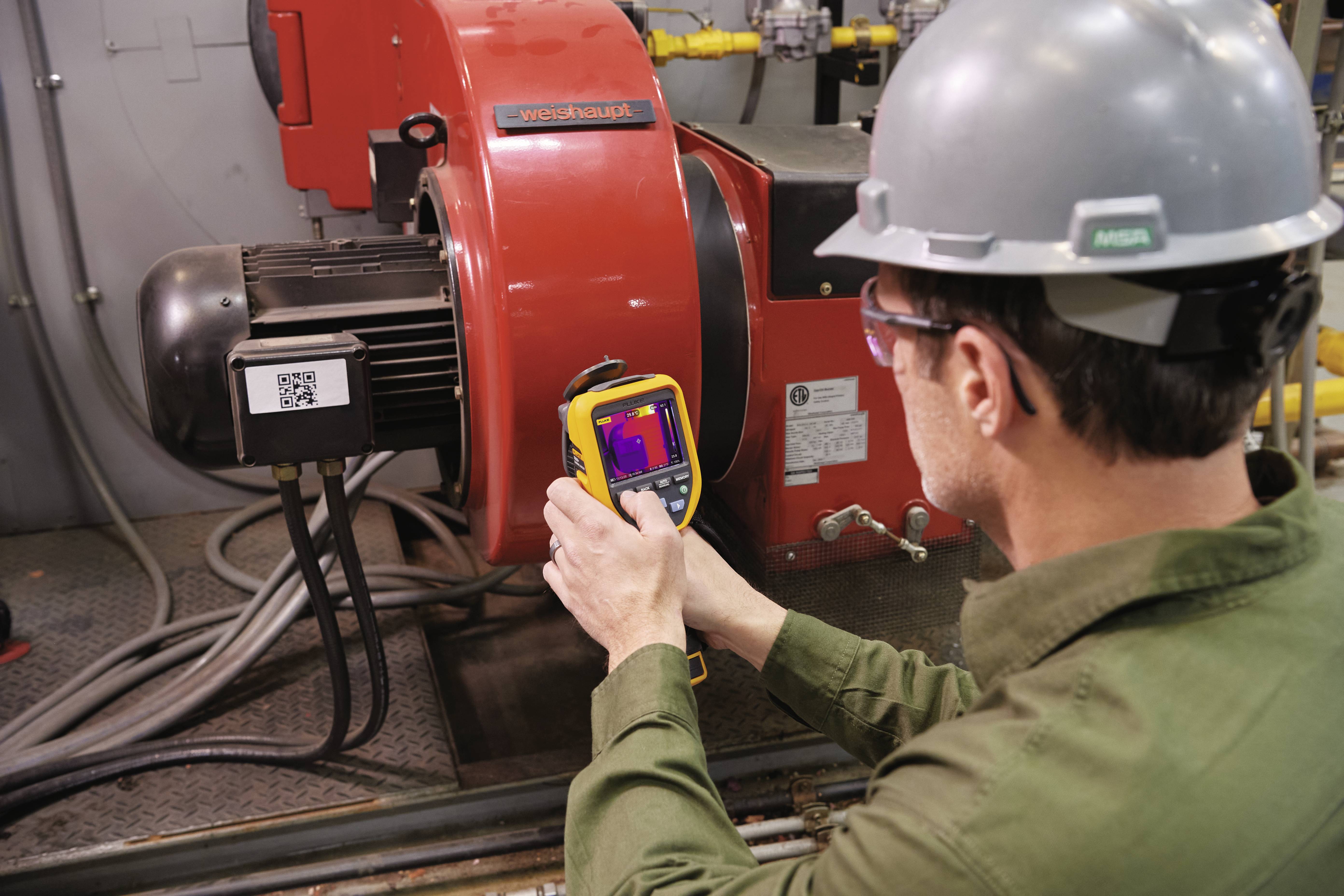 Un tecnico utilizza una termocamera per controllare la temperatura di un motore elettrico rosso. Il motore sta funzionando normalmente.