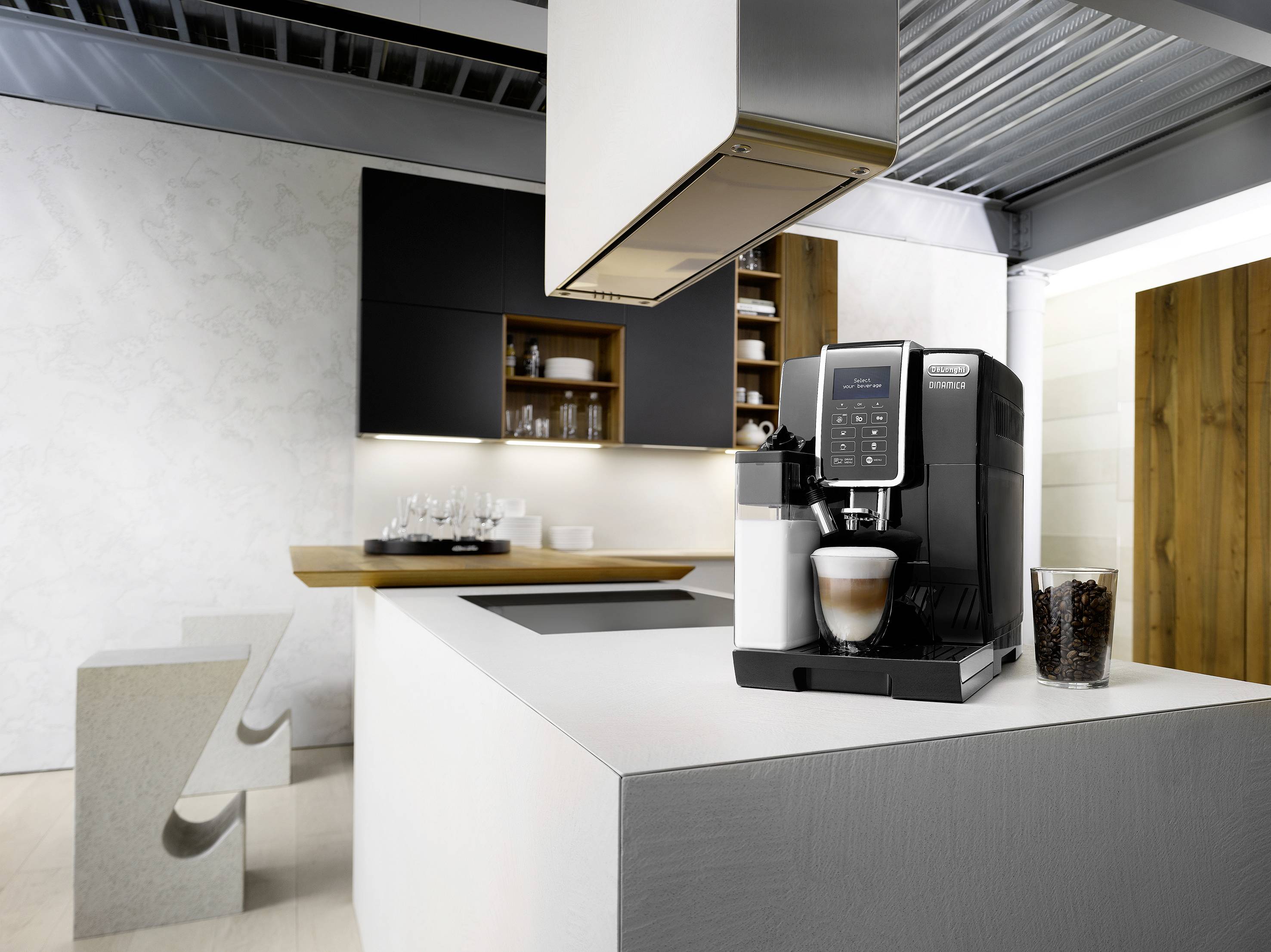 Una cucina moderna con una macchina da caffè nera sul piano di lavoro in primo piano. Sullo sfondo, scaffali aperti con stoviglie.