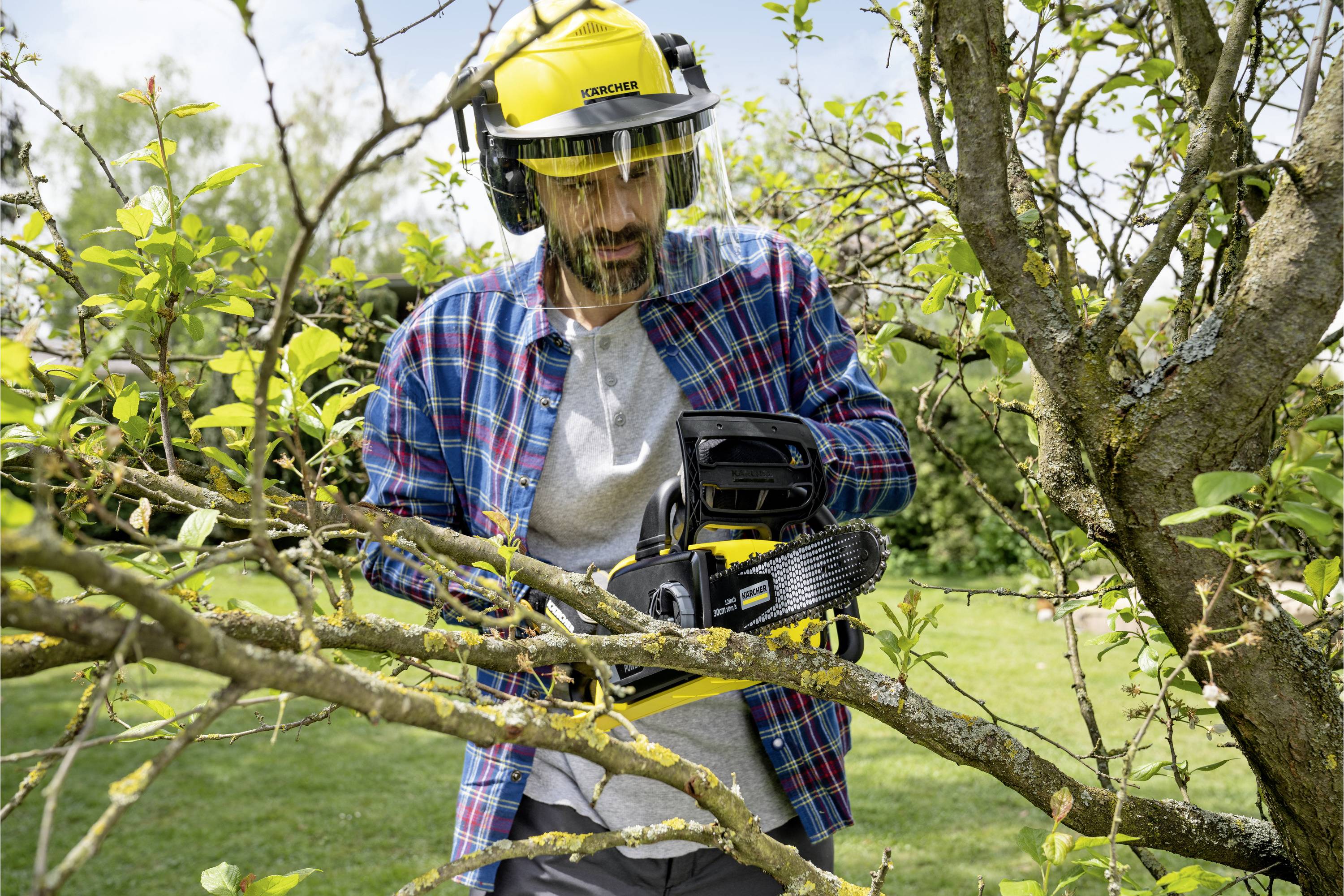 Un uomo con indumenti protettivi taglia rami da un albero con una motosega in un giardino.