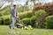 Un uomo taglia l'erba con un tosaerba giallo in un giardino verde in una giornata di sole.