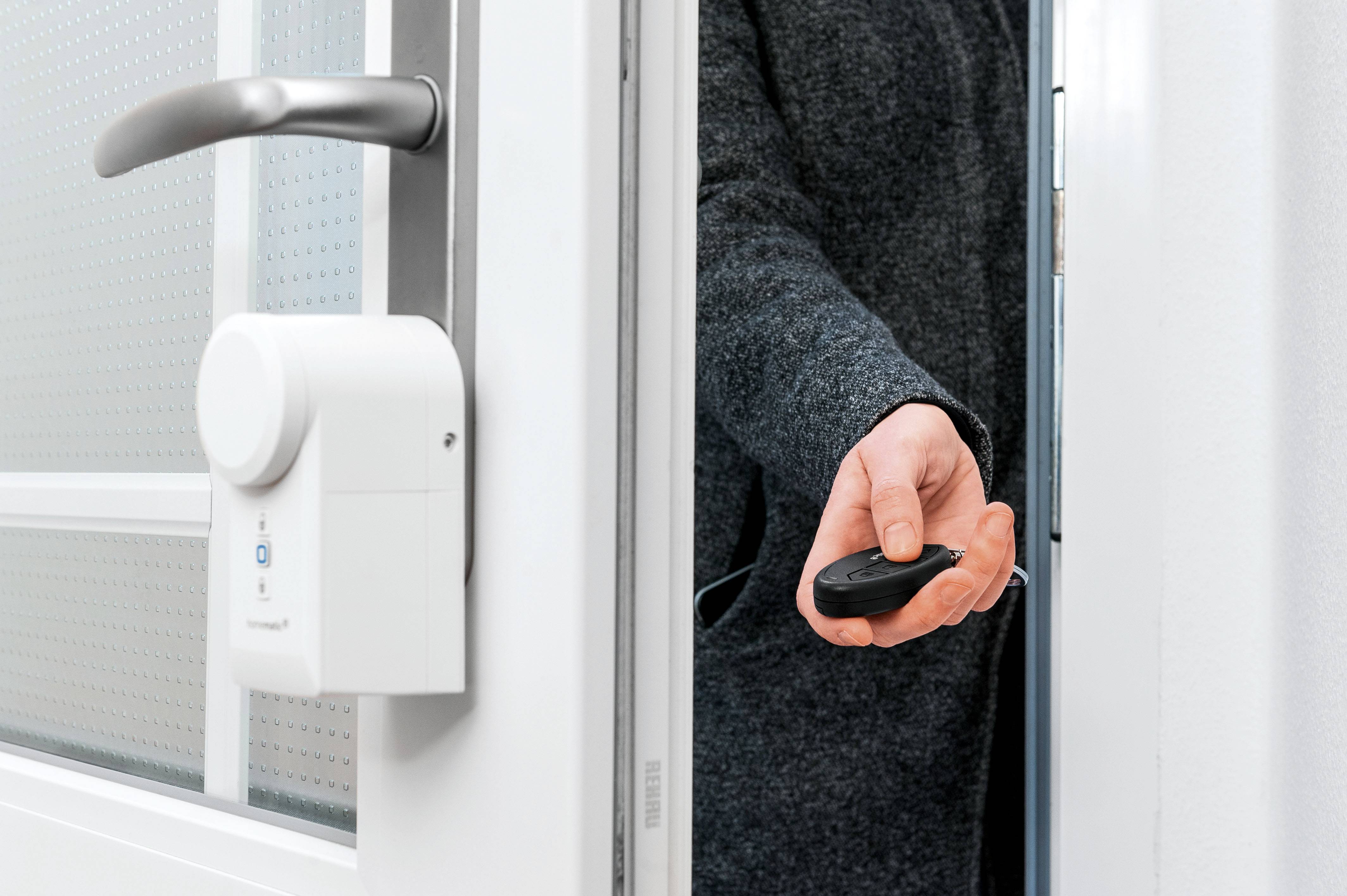 Una persona con un cappotto apre una porta con serratura elettronica, tenendo in mano un telecomando.