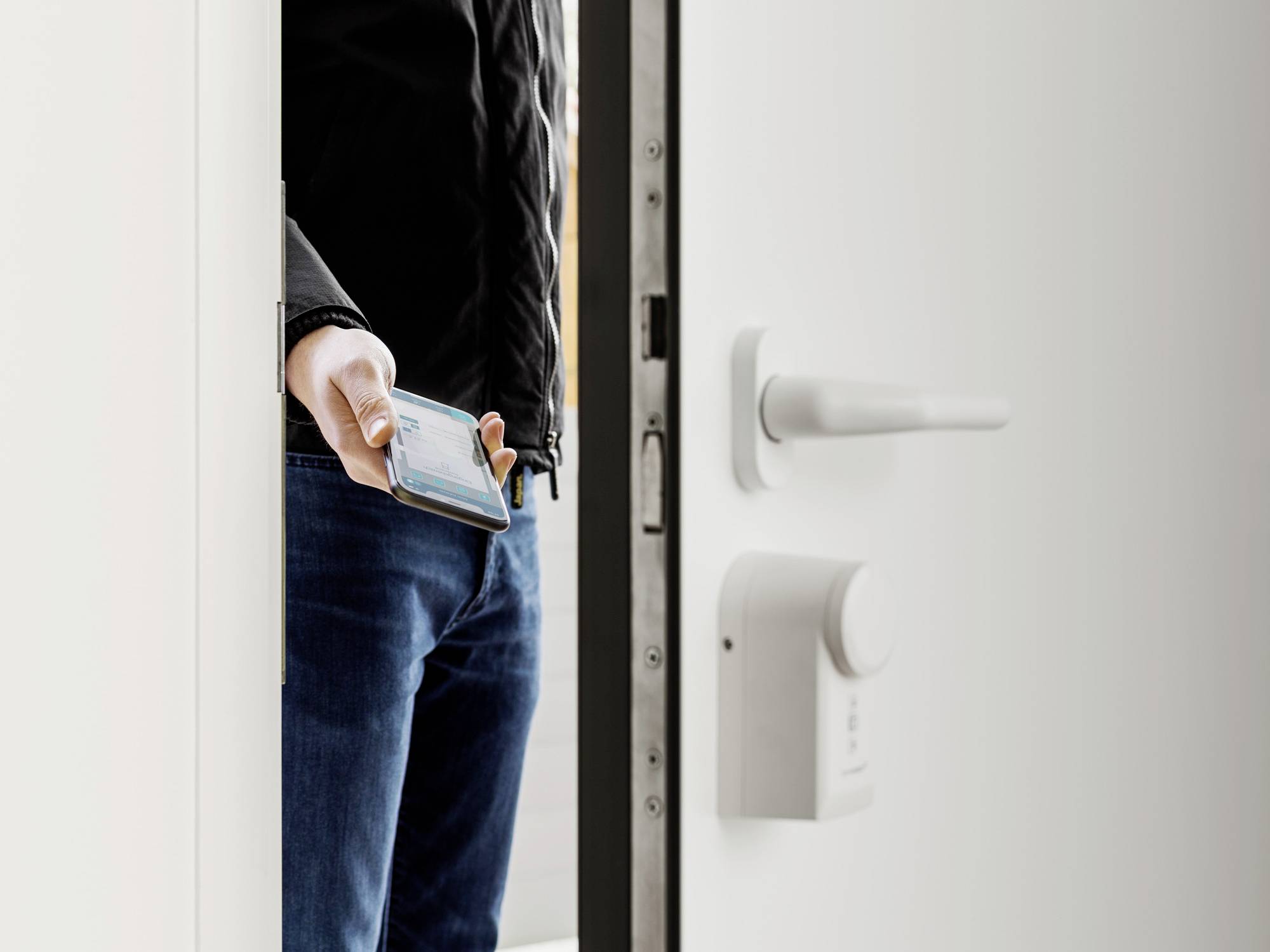 Una persona apre una porta tenendo in mano uno smartphone. Sulla porta è visibile una serratura elettronica.