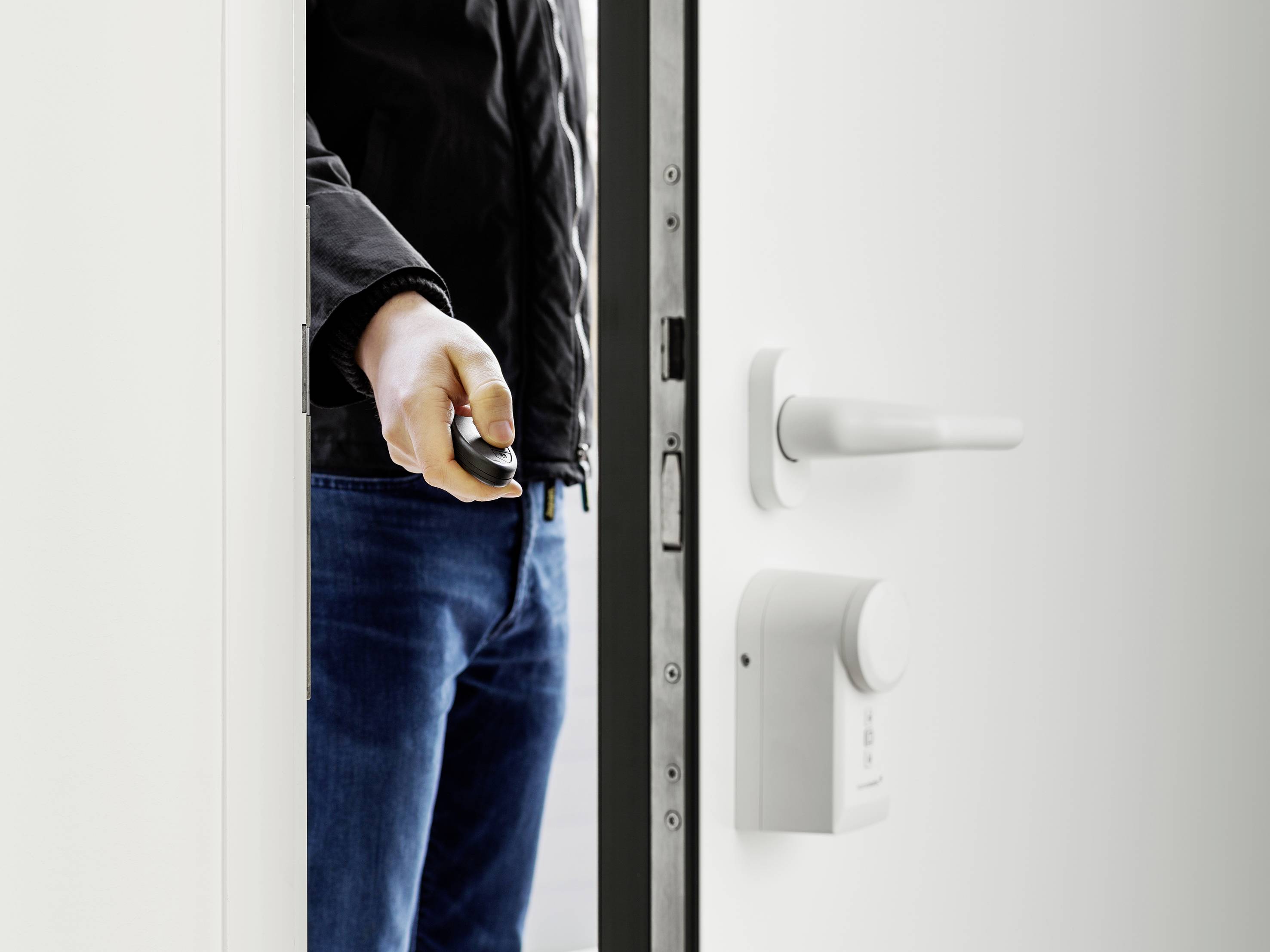 Una persona apre una porta bianca per uffici con un apriporta. Sulla porta è montata una serratura elettronica.