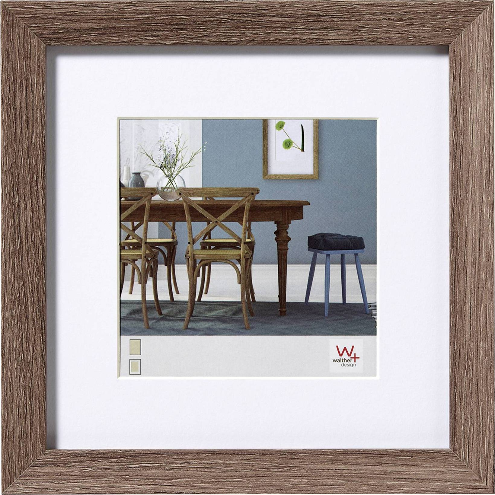 Sala da pranzo con tavolo in legno, quattro sedie e uno sgabello blu. Sulla parete un dipinto incorniciato e un vaso con rami sul tavolo.