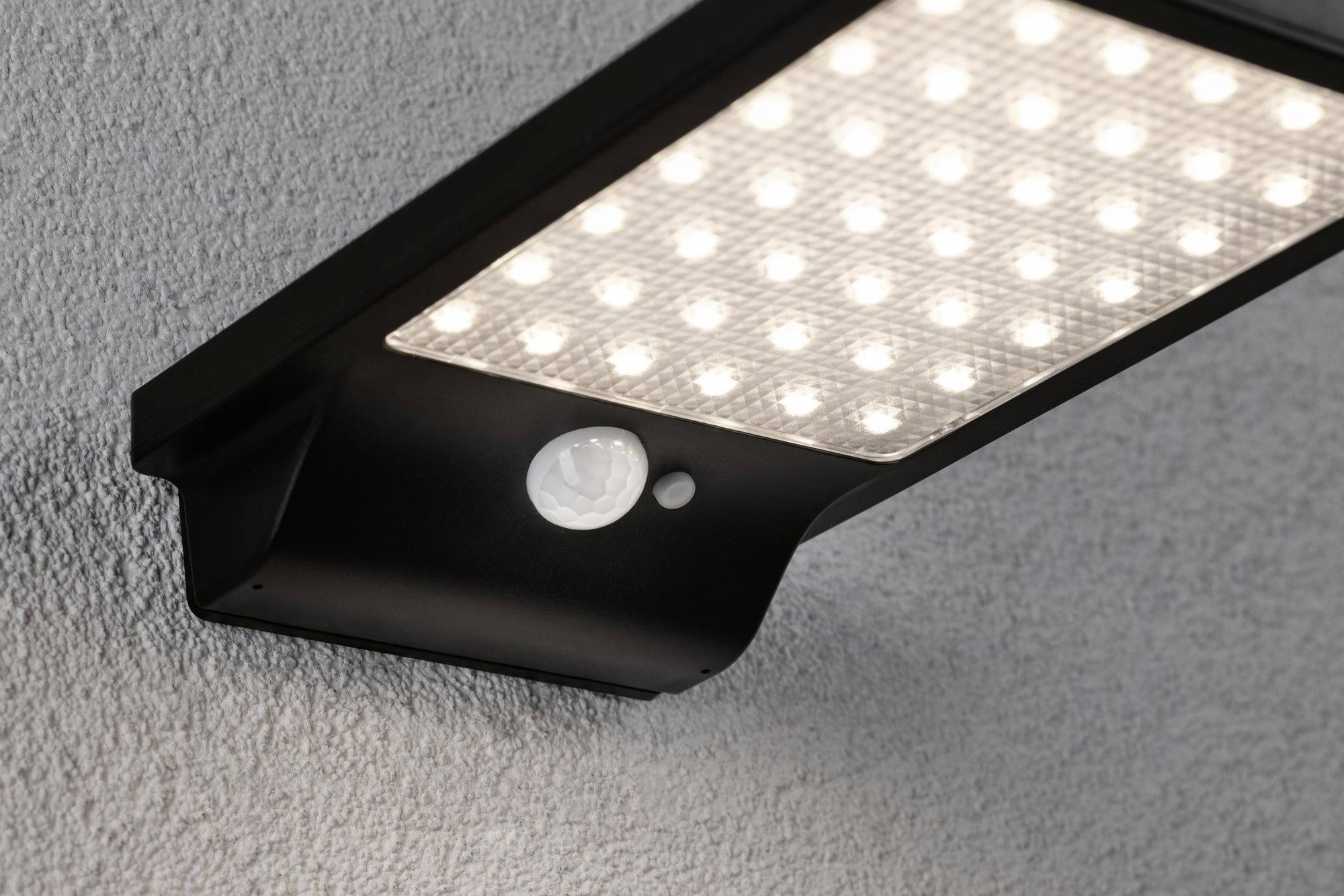 Una plafoniera LED nera con sensore di movimento montata su un soffitto bianco strutturato.