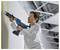 Una persona con indumenti di protezione utilizza un utensile elettrico per applicare del materiale lungo un giunto d'angolo in un cantiere edile. Sopra di essa è visibile la struttura del soffitto.