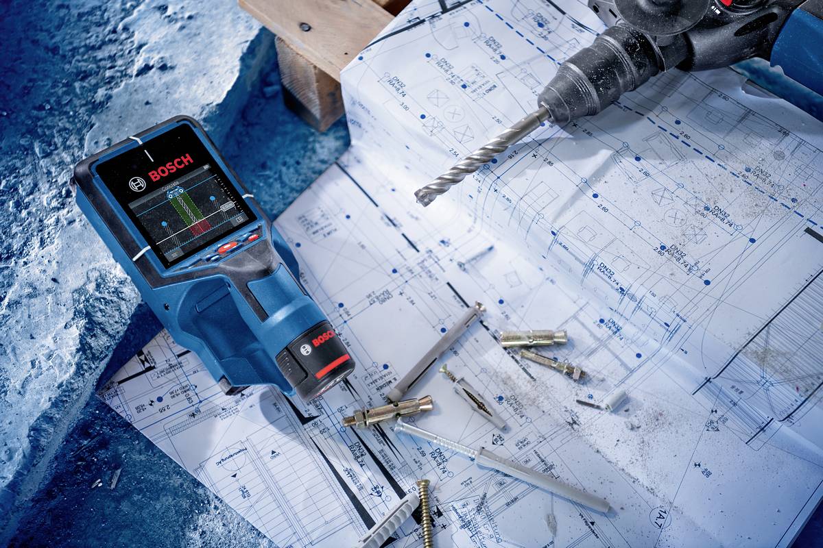 Un scanner Bosch è posizionato su piante di progetto accanto a un trapano e diverse viti. Situazione di cantiere con dettagli tecnici.