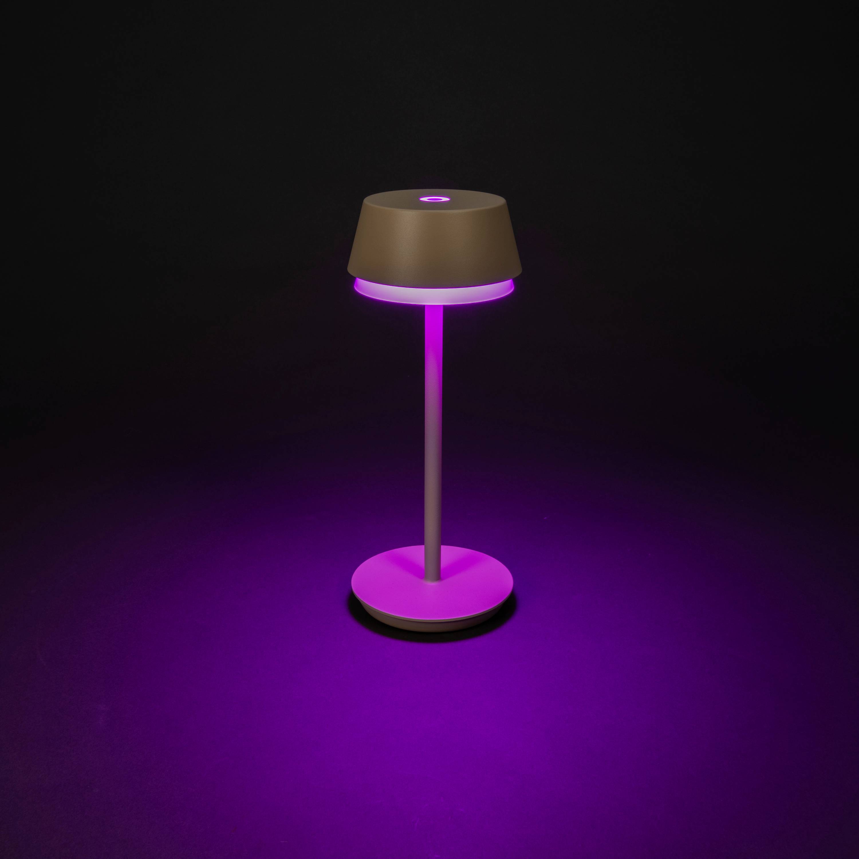 Una moderna lampada da tavolo illumina con luce viola, circondata dall'oscurità. La lampada ha una base rotonda e un paralume conico.