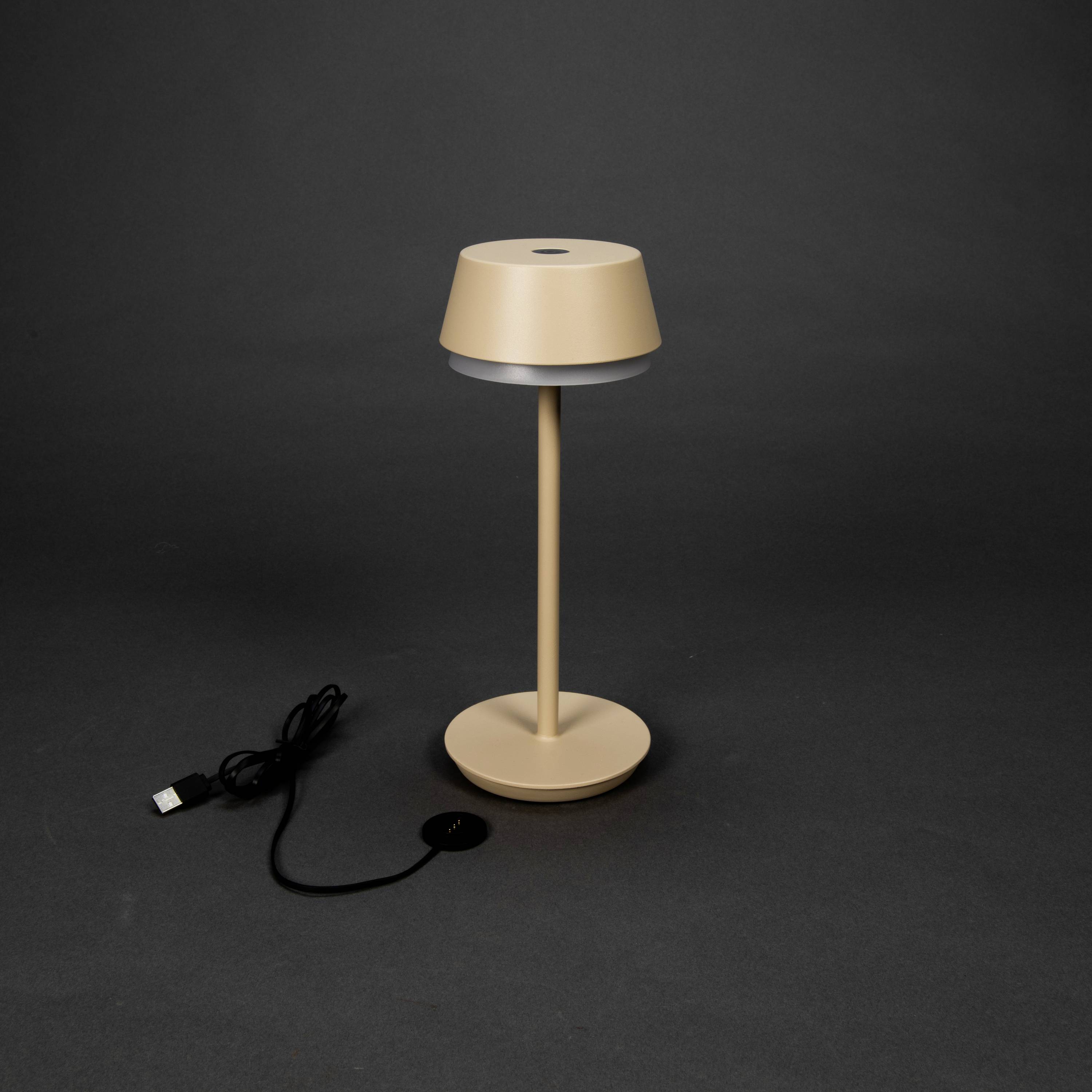 Lampada da tavolo beige con porta USB su sfondo scuro. Design moderno con paralume cilindrico su base sottile e slanciata.
