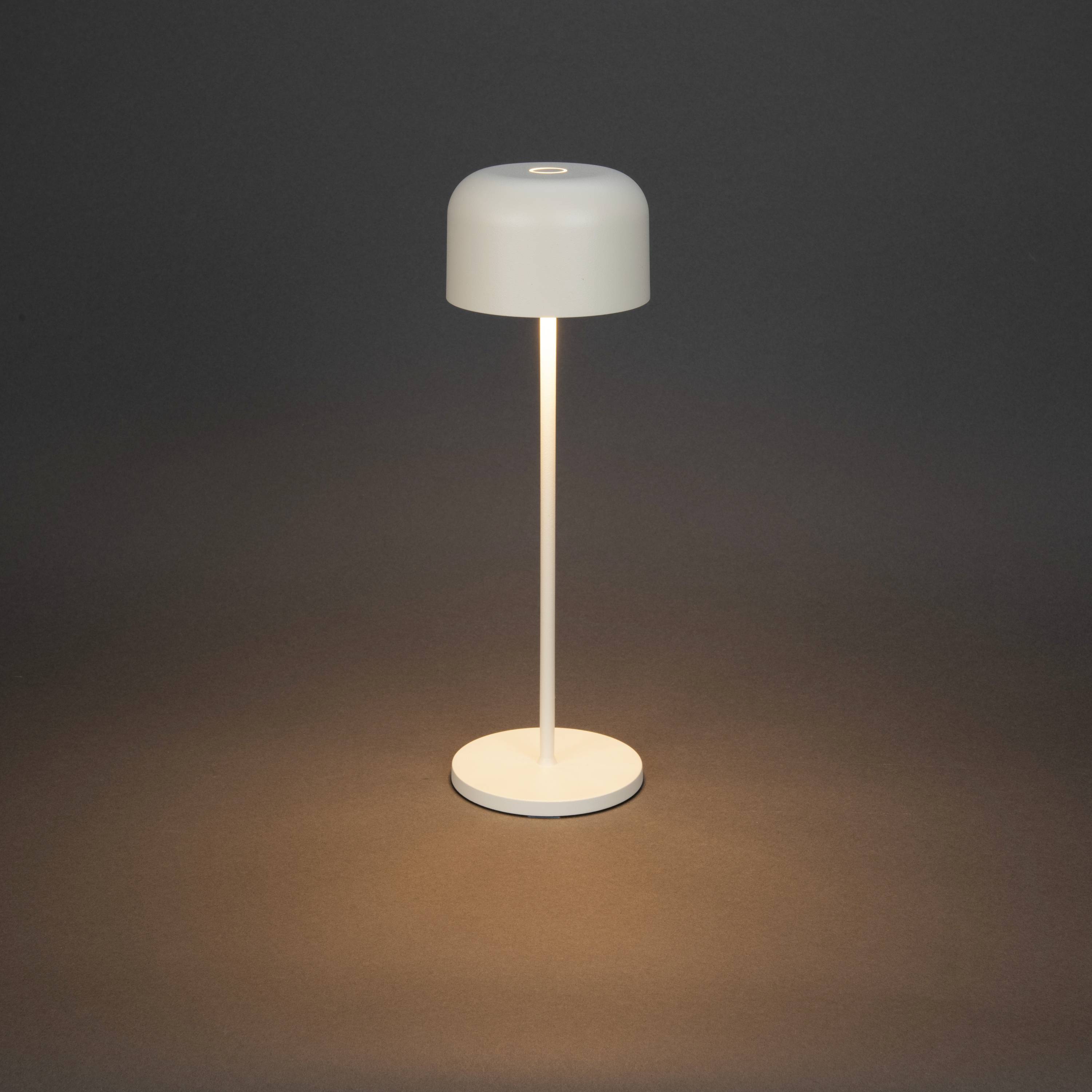 Una semplice lampada da tavolo con paralume rotondo che irradia una luce calda verso il basso, poggiata su uno sfondo scuro.