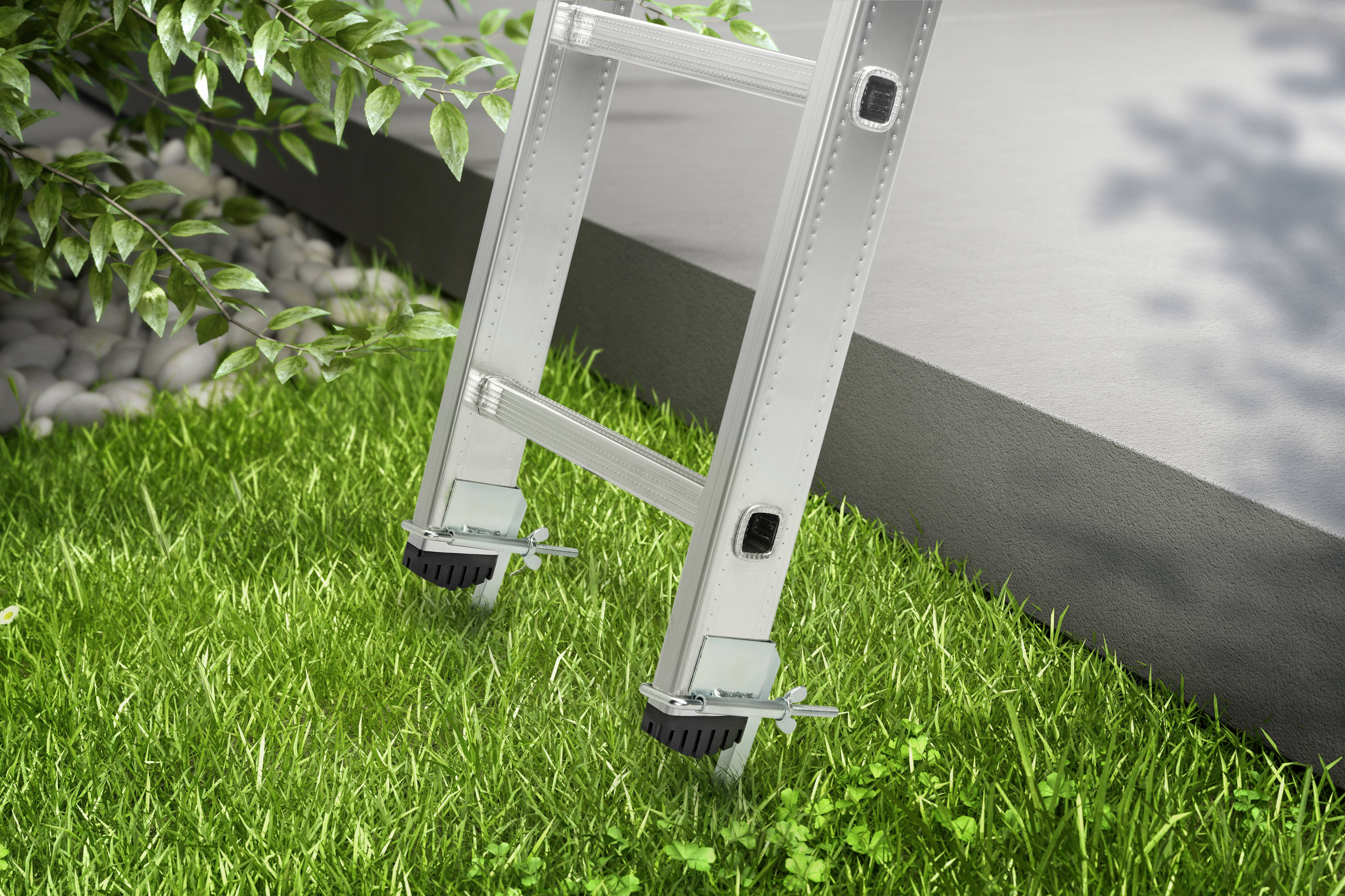 Una scala è posizionata stabilmente nell'erba verde e poggia su un piedistallo grigio in cemento. Cespugli e pietre sono visibili sullo sfondo.