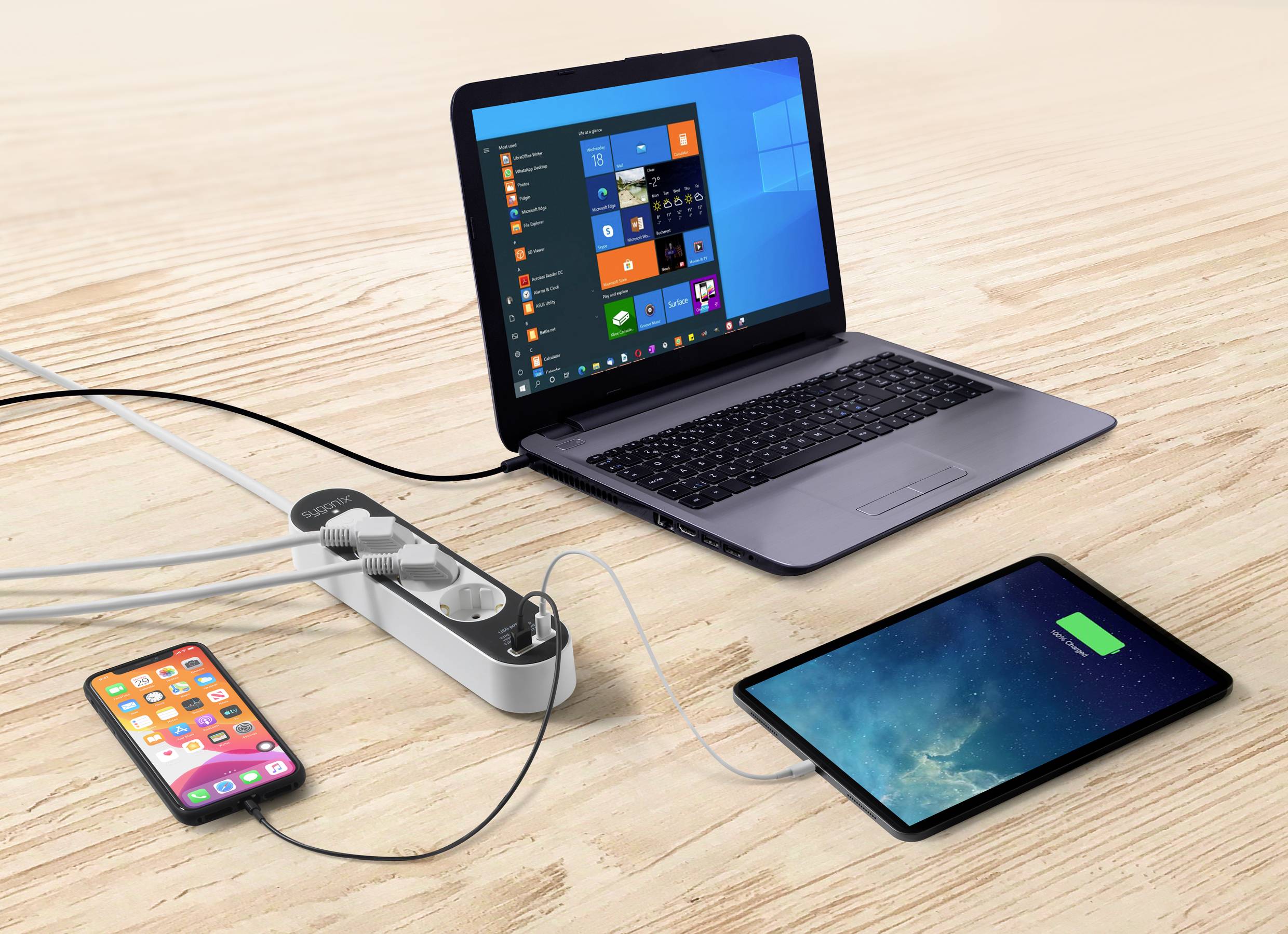 Un laptop, un tablet e uno smartphone sono collegati e in carica tramite un cavo di prolunga su un tavolo di legno.