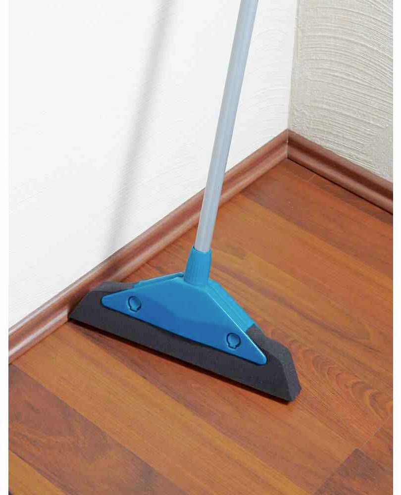 Un panno blu pulisce una listella di legno color mogano su un pavimento di legno, vicino a un angolo di una parete bianca.