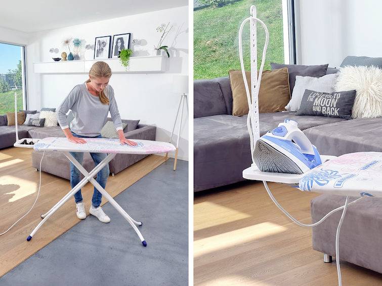 Una donna sta stirando dei vestiti su un asse da stiro in un soggiorno con un divano e dei cuscini. Ambiente luminoso e moderno con una grande vetrata.