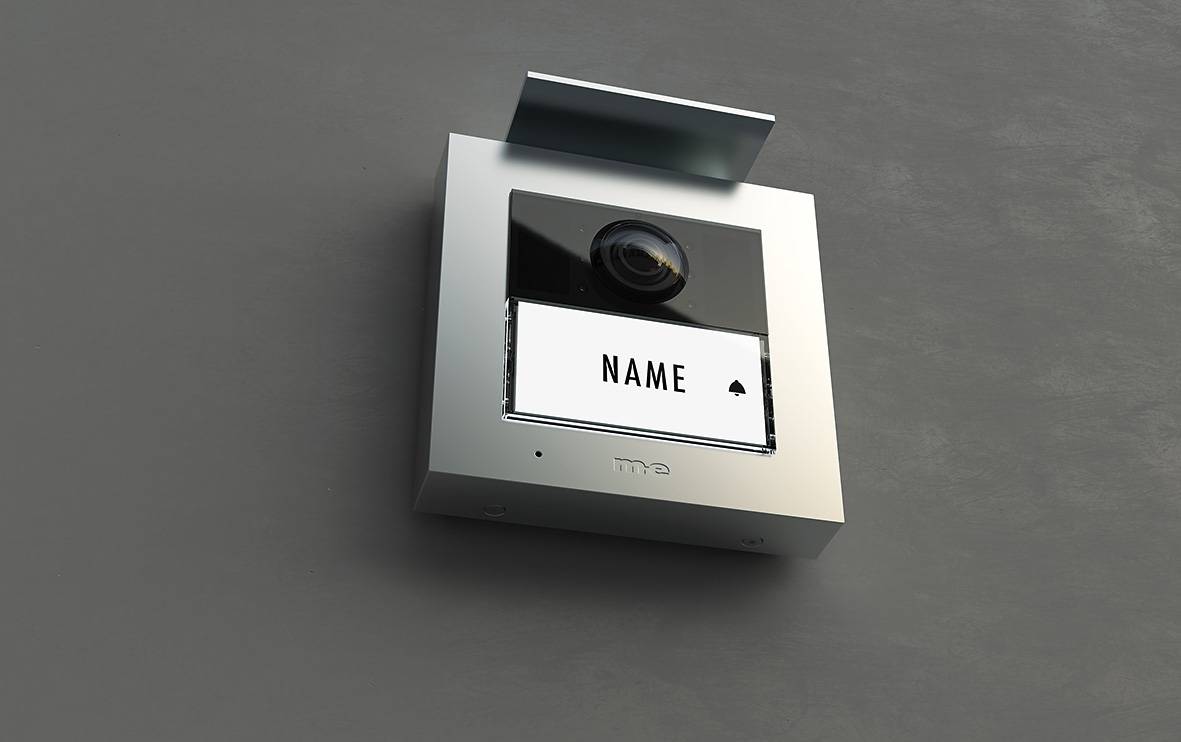 Interfono in argento fissato a una parete, con un ampio display e una telecamera. Il display mostra 'NOME'.