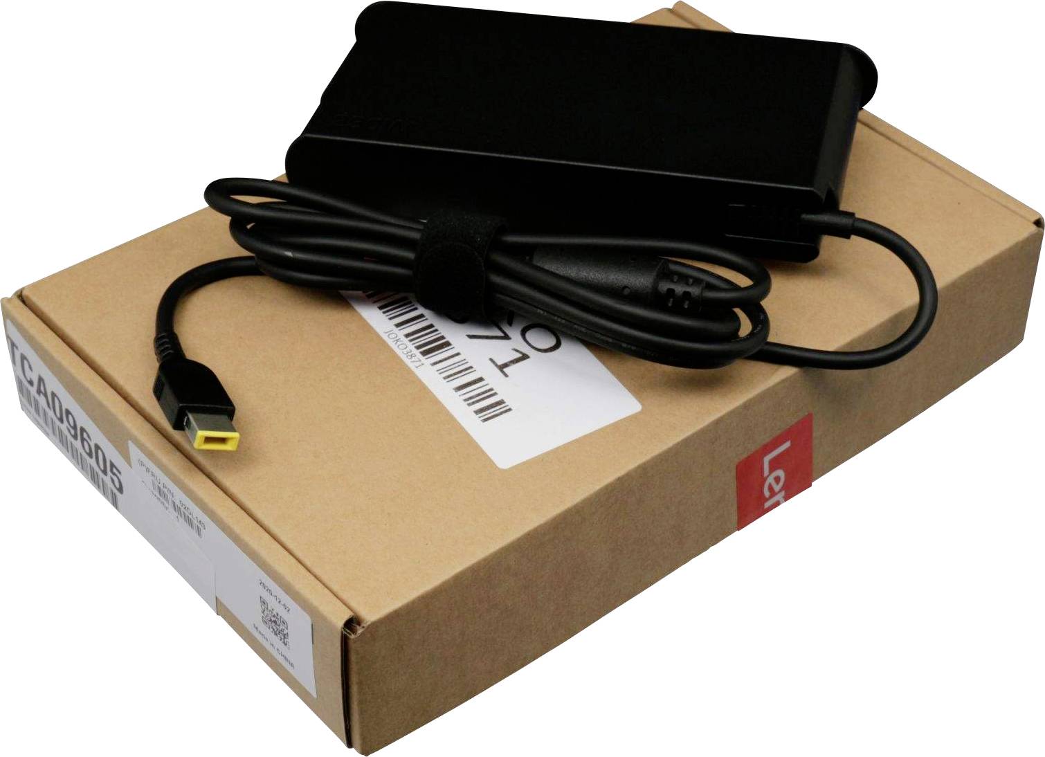 Un alimentatore nero per laptop è poggiato su una scatola marrone. Il cavo è avvolto ordinatamente, e un'estremità gialla è visibile.
