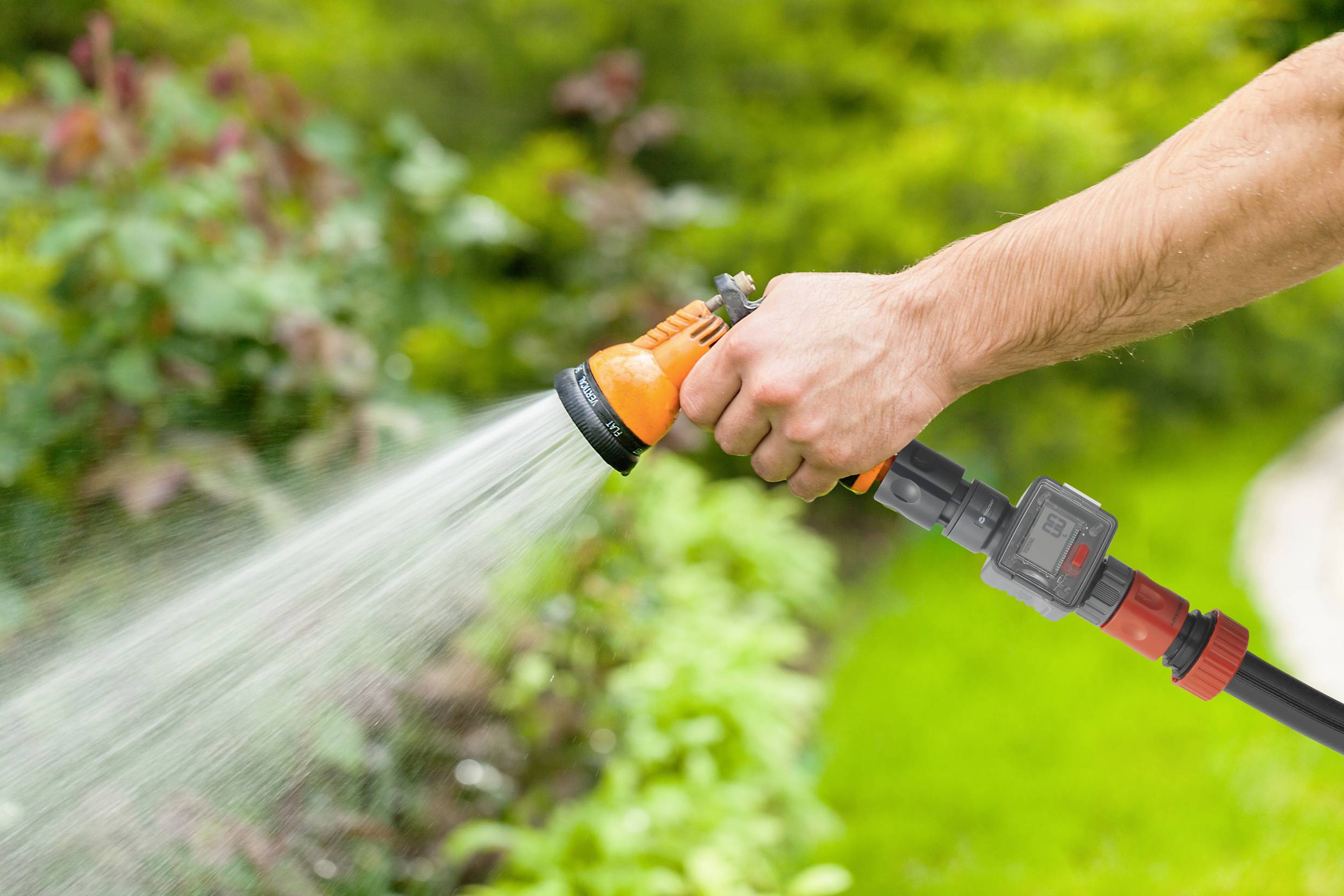 Una persona tiene un tubo da giardino e innaffia le piante in un giardino verde.