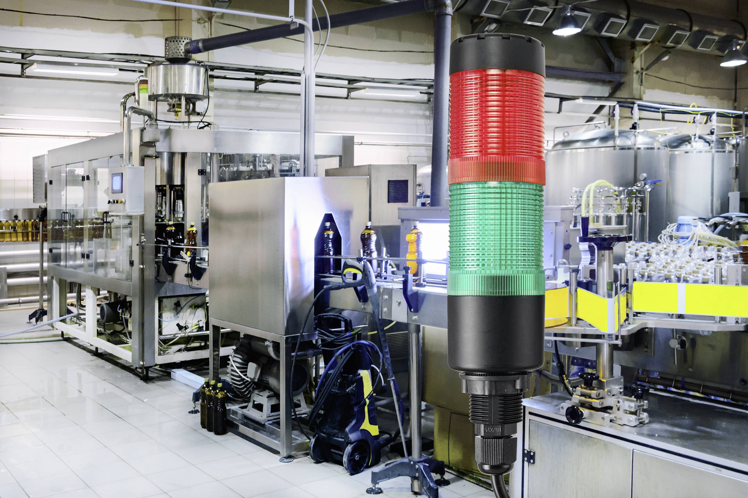 Impianto di produzione automatizzato con una torre di segnalazione a tre colori in primo piano, che mostra segnali di stato.