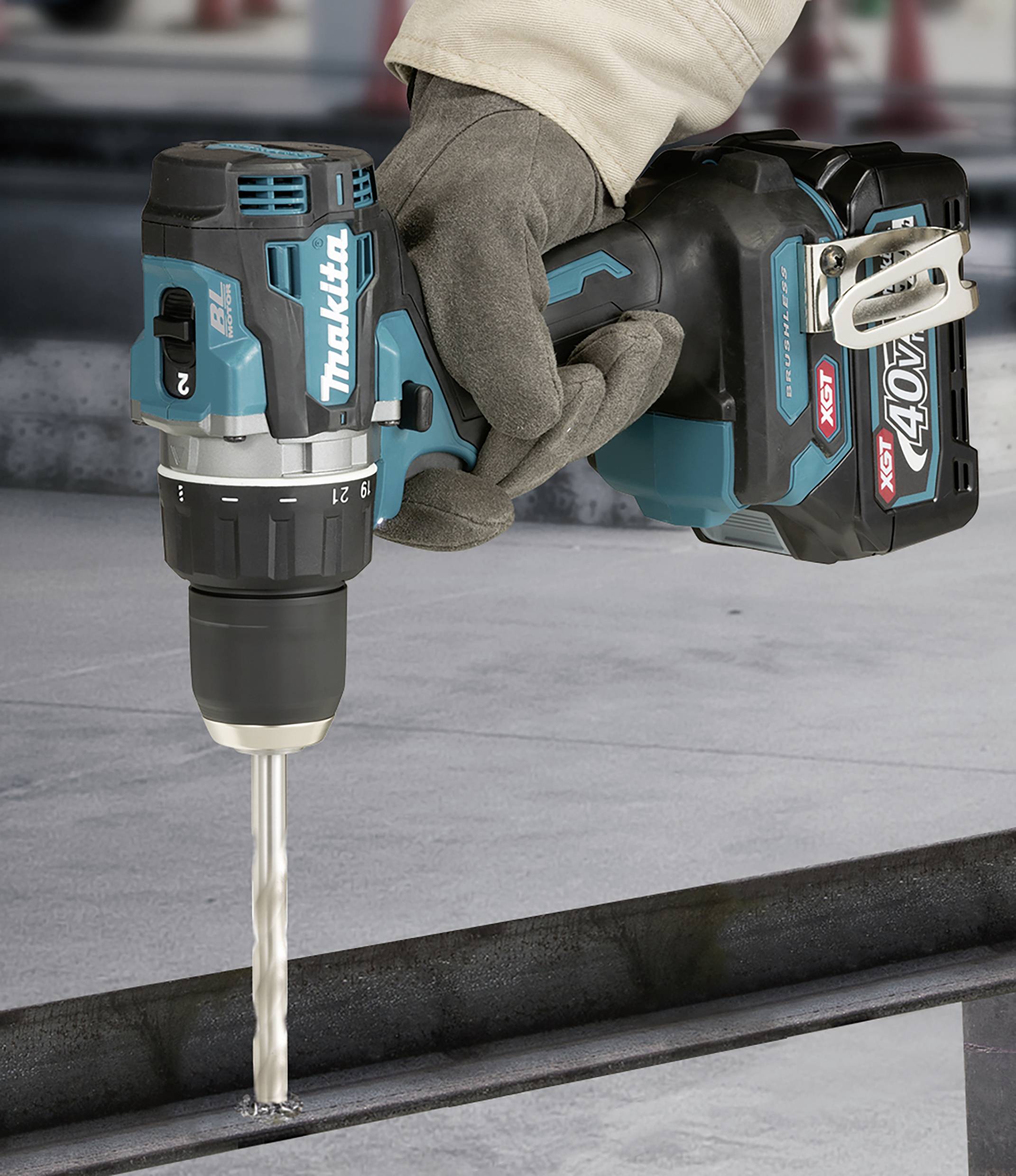 Un lavoratore con i guanti sta usando un avvitatore a batteria blu per forare un pezzo di metallo.