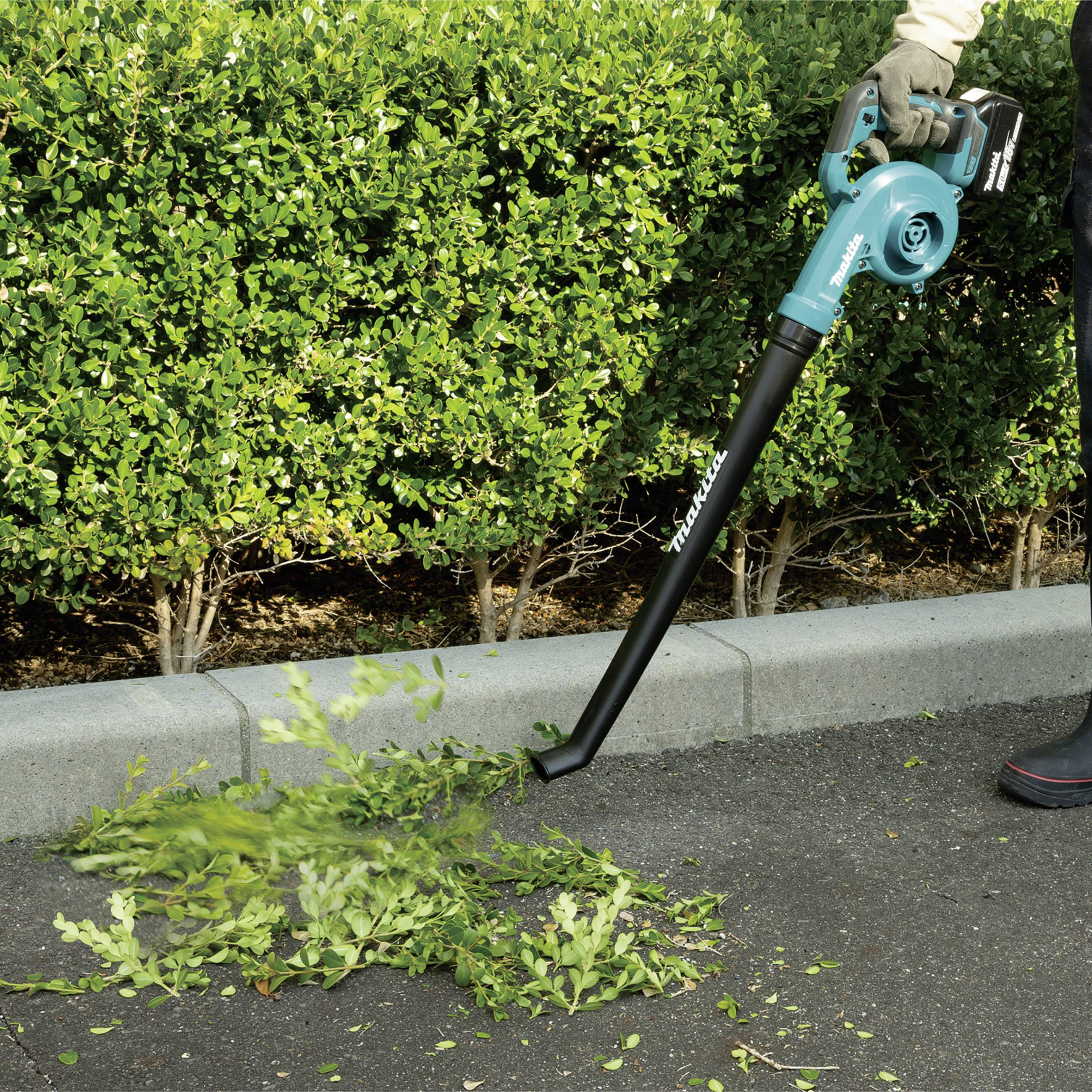 Una persona sta utilizzando un soffiatore per rimuovere foglie e rami da una superficie pavimentata e spostarli sul prato.