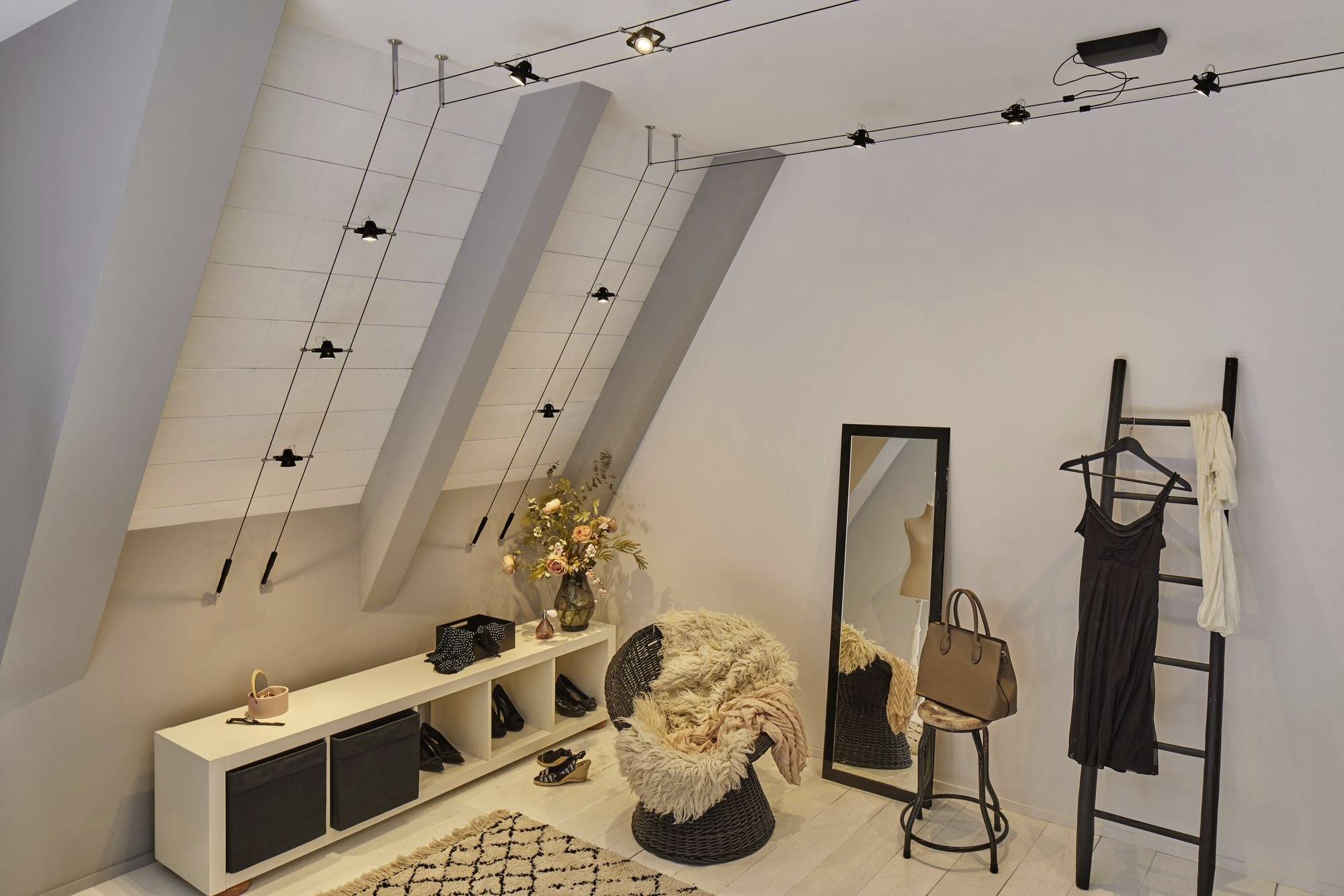 Un moderno spogliatoio con tetto inclinato, specchio, scala utilizzata come appendiabiti, poltrona, insieme a capi di abbigliamento eleganti e accessori.