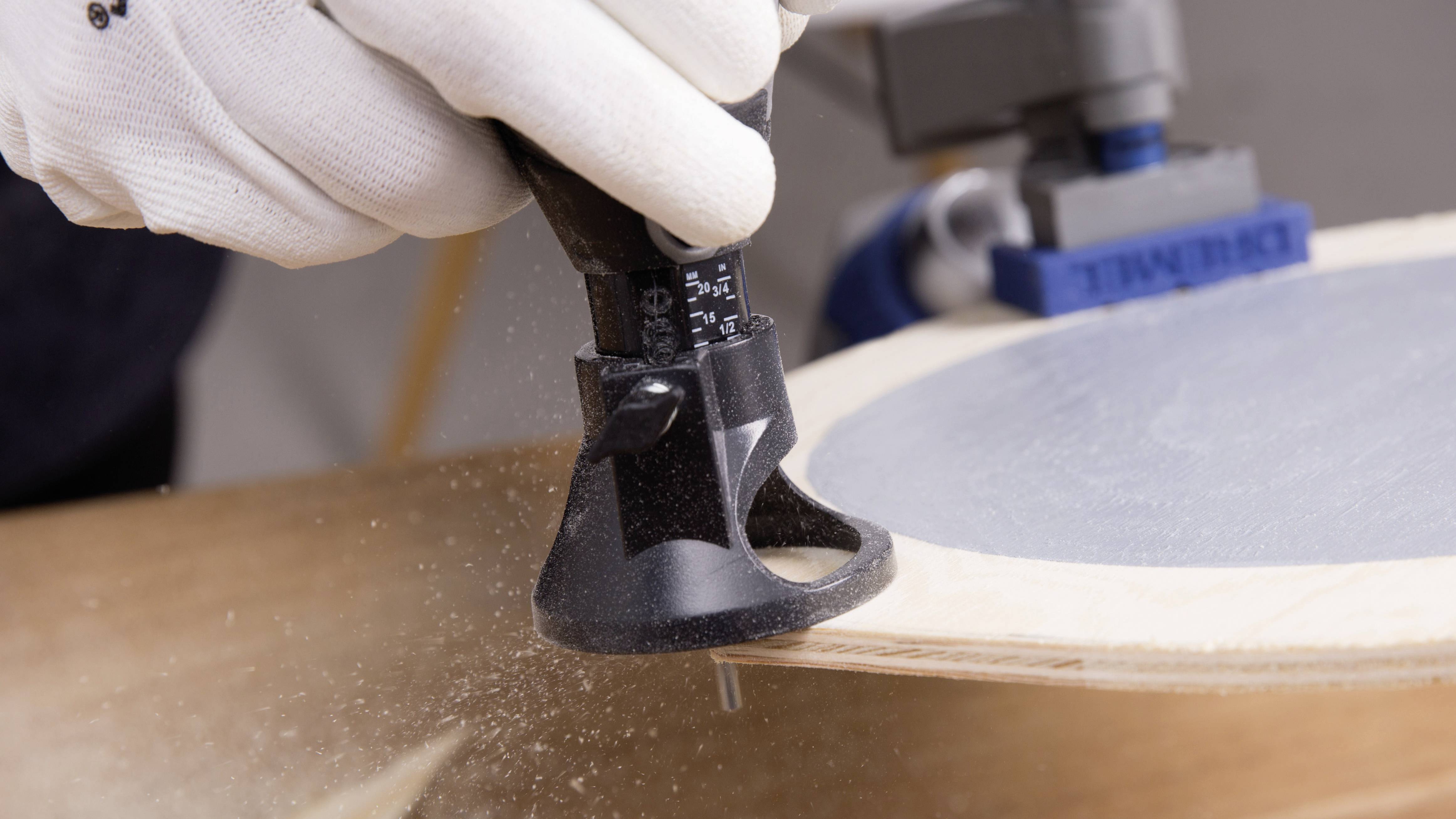 Una persona sta fresando una tavola di legno con un utensile multifunzione. Trucioli di legno volano nell'aria. L'utensile e il legno sono al centro dell'inquadratura.