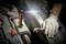 Una persona con i guanti sta riparando un motore all'interno di un'auto. Una lampada da lavoro illuminata rischiara l'area.