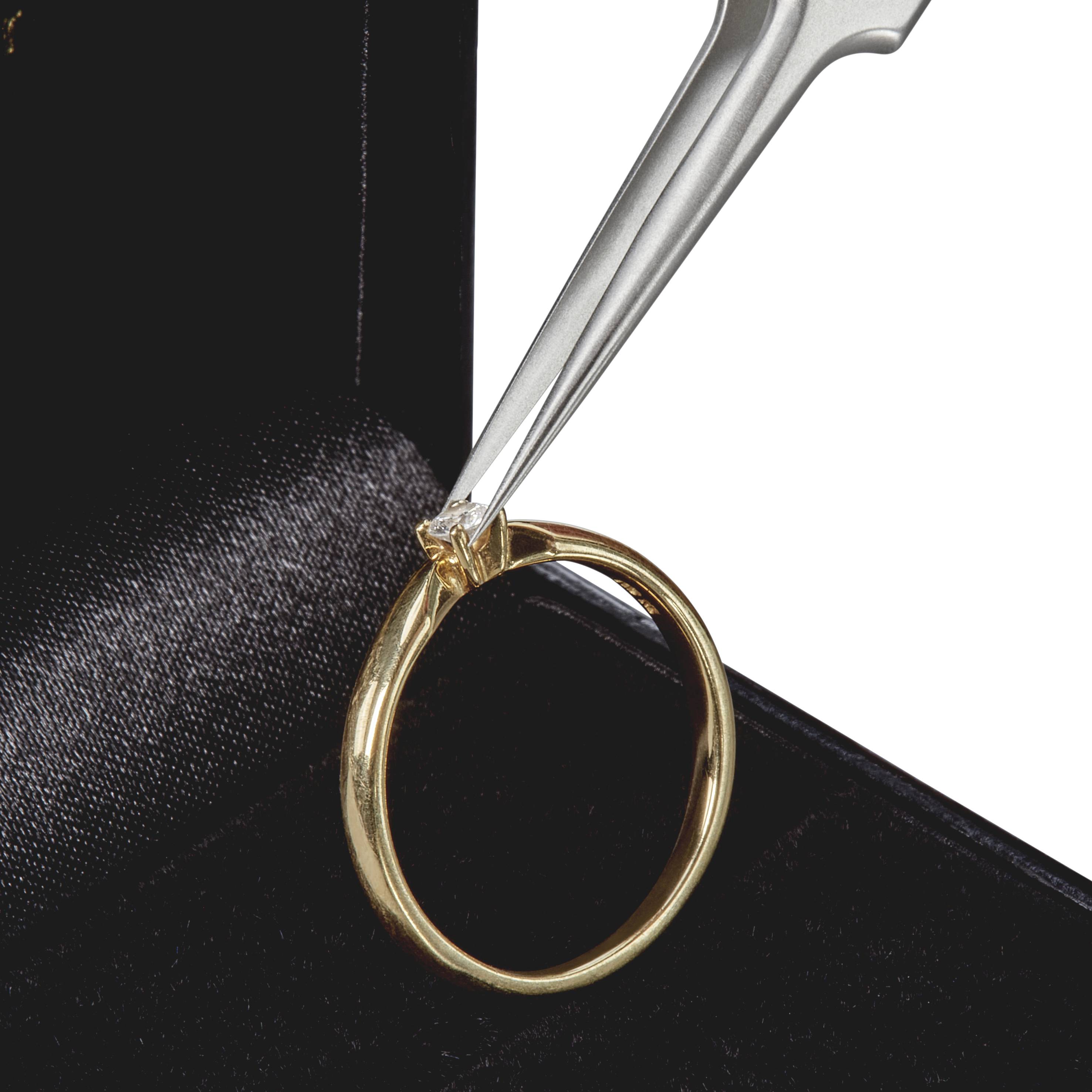 Un anello d'oro viene tenuto con una pinzetta d'argento da un cofanetto dei gioielli.