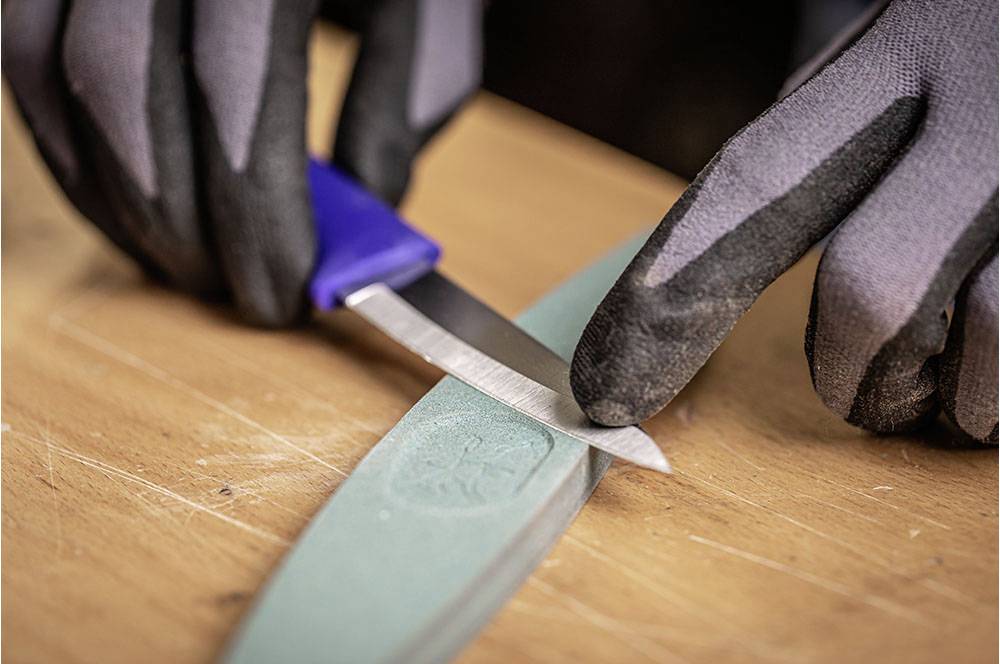 Una persona sta affilando un coltello su una mola. Indossa guanti neri.