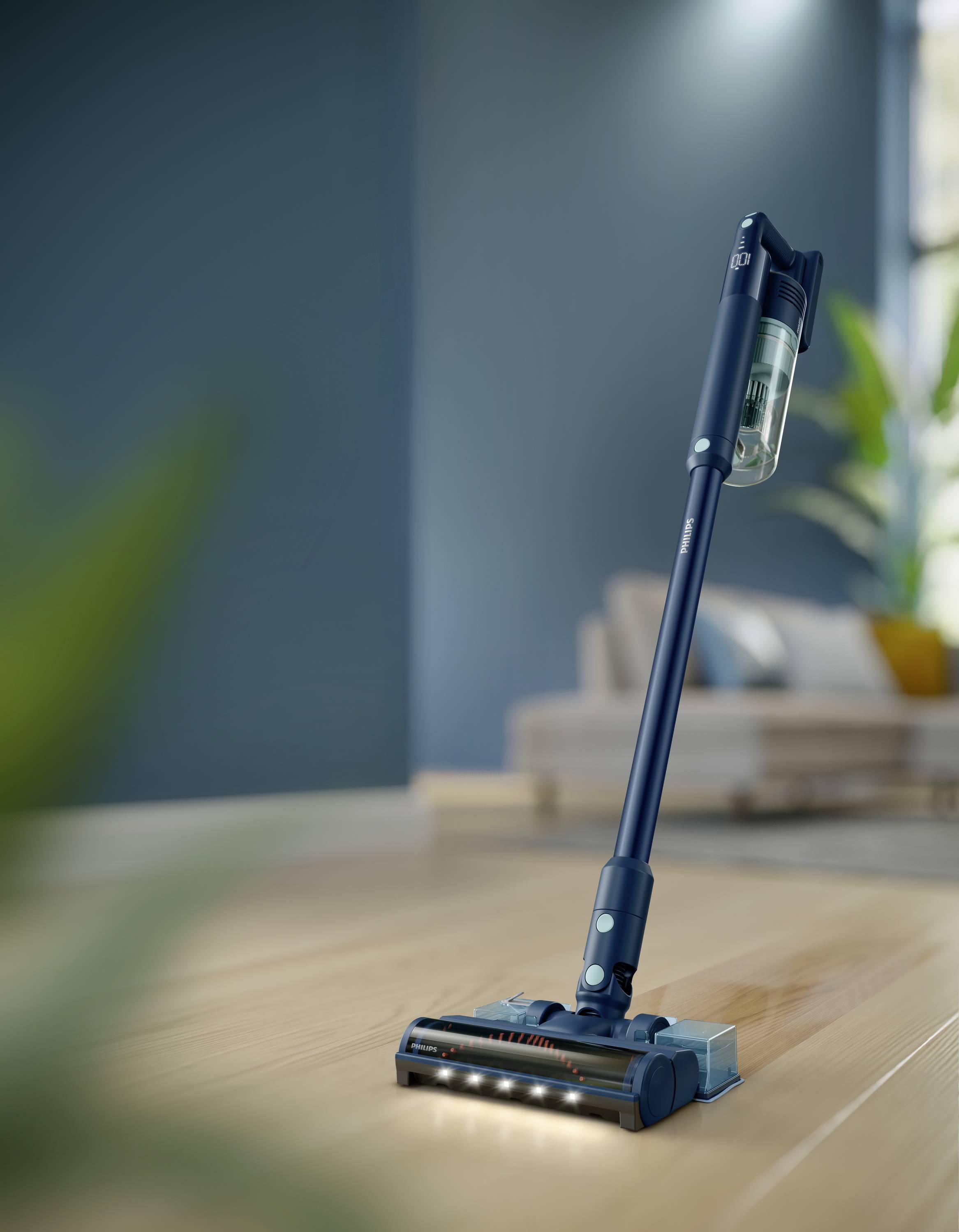 Un aspirapolvere wireless blu su un pavimento in legno in un soggiorno moderno con un divano sullo sfondo.