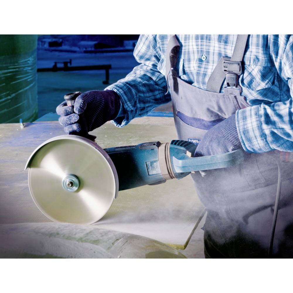 Una persona indossa indumenti protettivi e utilizza una smerigliatrice angolare per tagliare il metallo. Scintille e polvere circondano l'area di lavoro.