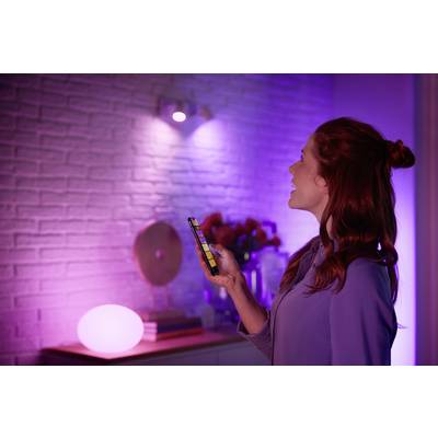 Una persona controlla l'illuminazione di una stanza con uno smartphone, dove l'ambiente è illuminato in tonalità viola e rosa.