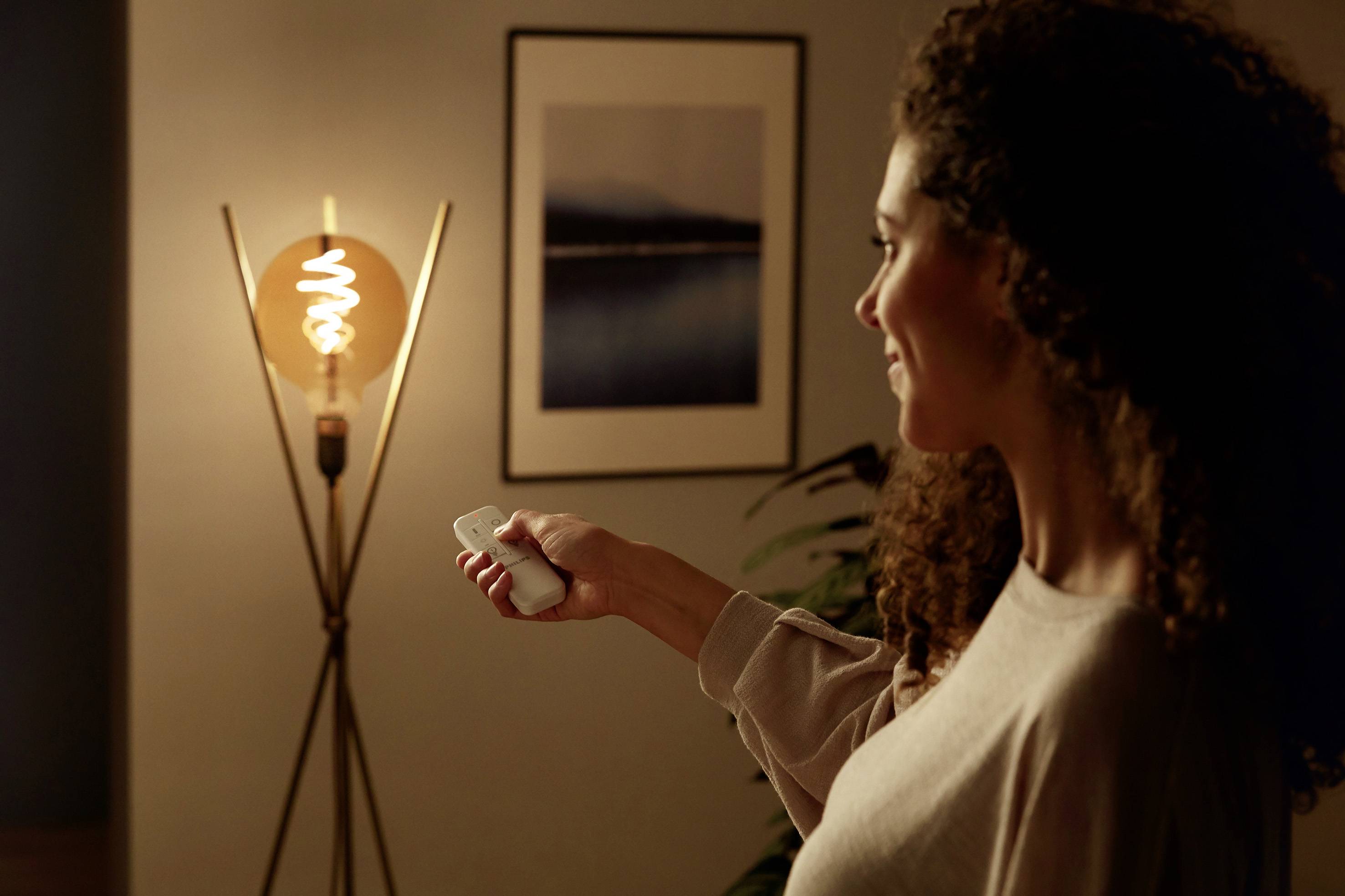 Una donna aziona con un telecomando una lampada da terra con una lampadina illuminata in un ambiente accogliente.