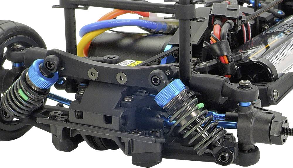 Primo piano di un'auto radiocomandata che mostra il sistema di sospensione con ammortizzatori blu e un motore elettrico cablato sullo sfondo.