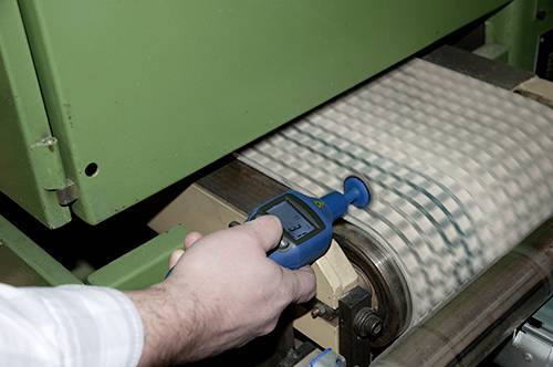 Una mano tiene uno strumento di misurazione sopra un rotolo di carta verde con strisce blu. Lo strumento mostra un display digitale.