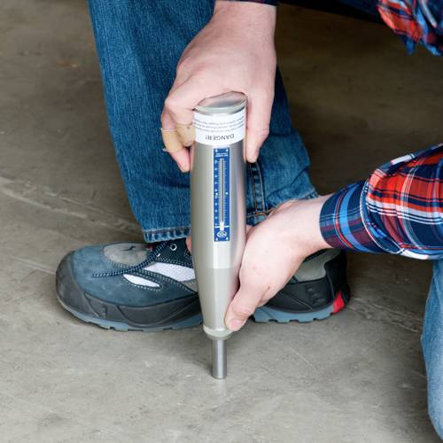 Una persona tiene un martello per prove di durezza del calcestruzzo sopra una superficie in calcestruzzo. Il martello viene utilizzato per verificare la resistenza del calcestruzzo.