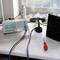 Un dispositivo di misurazione con display digitali mostra valori accanto a una presa elettrica, un cacciavite e una bomboletta spray su un tavolo.