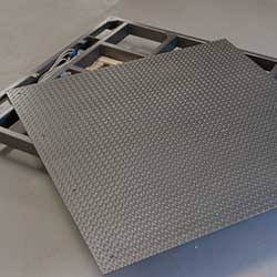 Un pezzo di fibra di carbonio grigio giace su un pallet con utensili sullo sfondo.