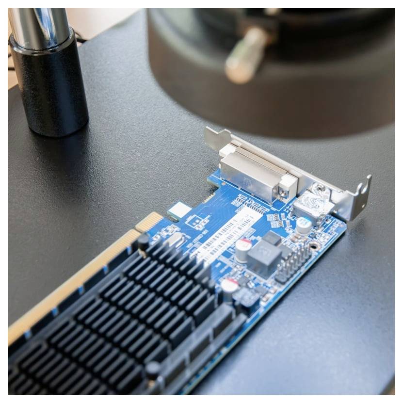 Primo piano di una scheda di espansione per computer blu con un grande dissipatore di calore nero e una staffa metallica su una scrivania, sotto un microscopio o uno strumento di ispezione.