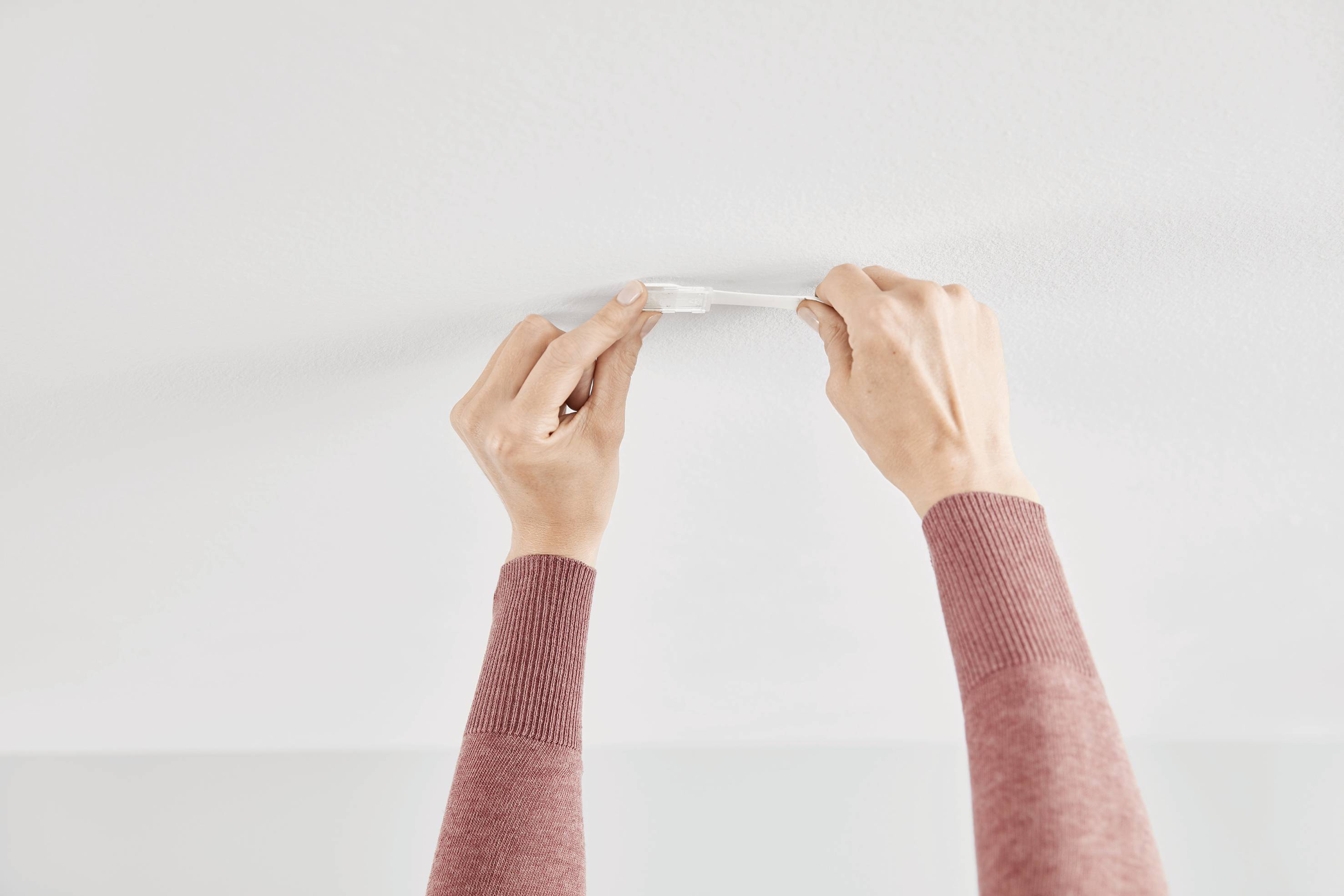 Mani di una persona che installa un rilevatore di fumo su un soffitto.