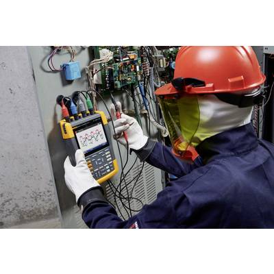 Un tecnico con casco e maschera protettivi sta verificando circuiti elettrici con un oscilloscopio all'interno di un quadro elettrico.