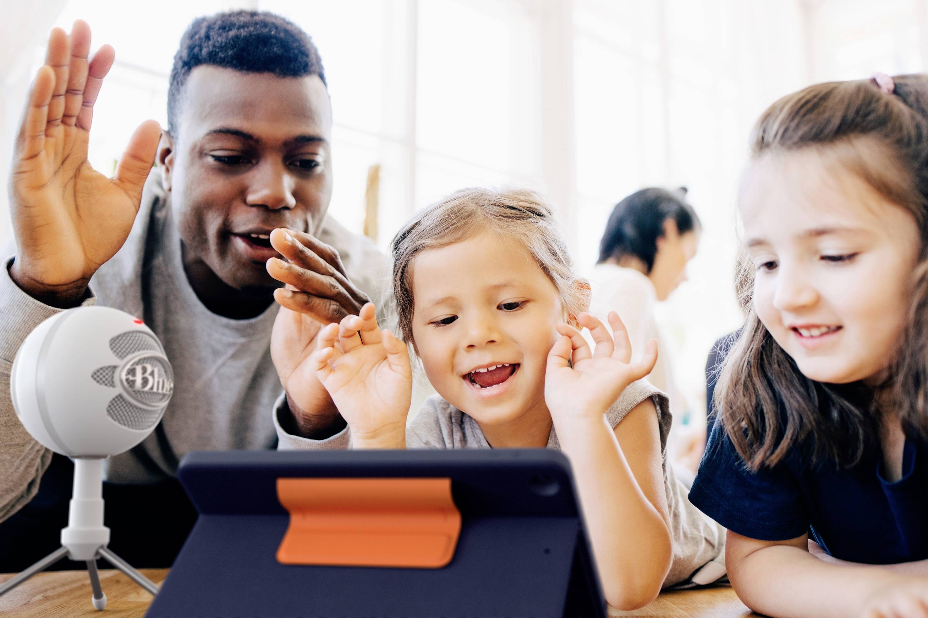 Un uomo e due bambini interagiscono allegramente con un tablet e un microfono. Sembrano partecipare a un gioco di apprendimento digitale.